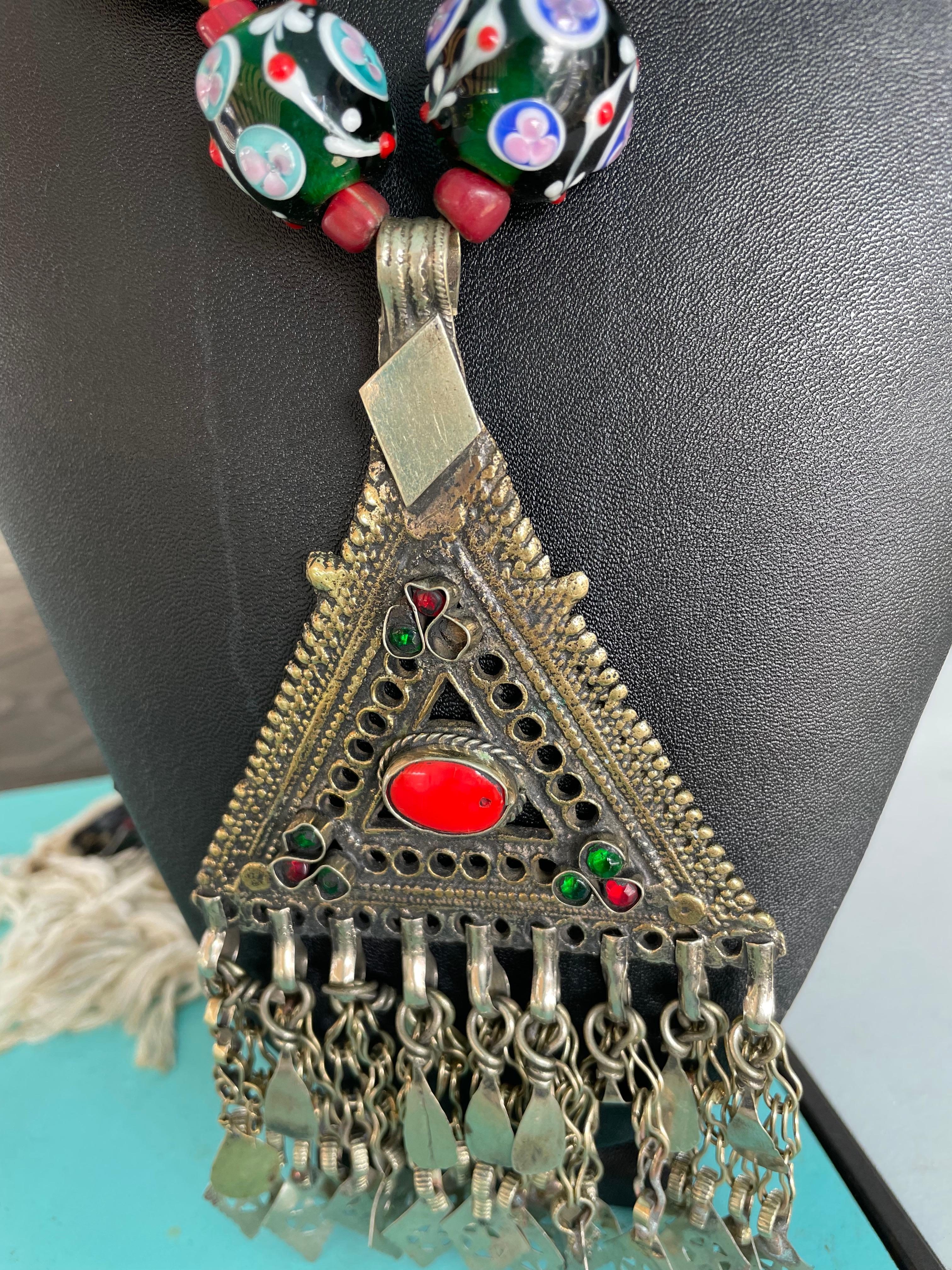 Lorraine’s Bijoux offers a one of a kind,handmade, statement necklace with a large vintage pendant from Afghanistan. This pendant has an inlaid coral stone and pieces of glass set into it.The beads consist of vintage hand painted ceramic beads also