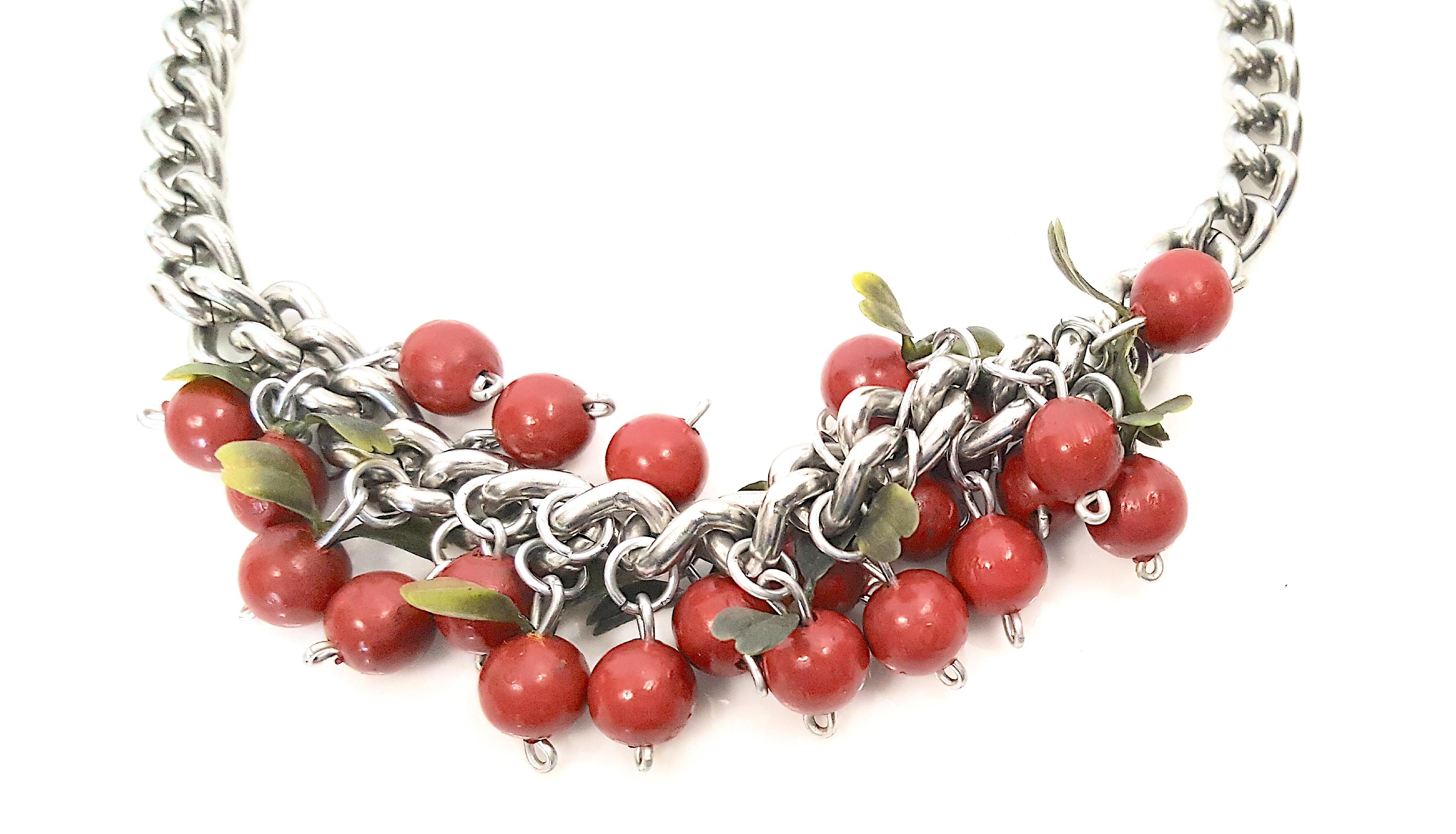This vintage cherry-fruit charm necklace featuring red hand-painted wood is constructed of silver chain links. The clasp extension-chain is decorated with a single red bead. The green leaves that trim the fruit beads are a surprising two-tone