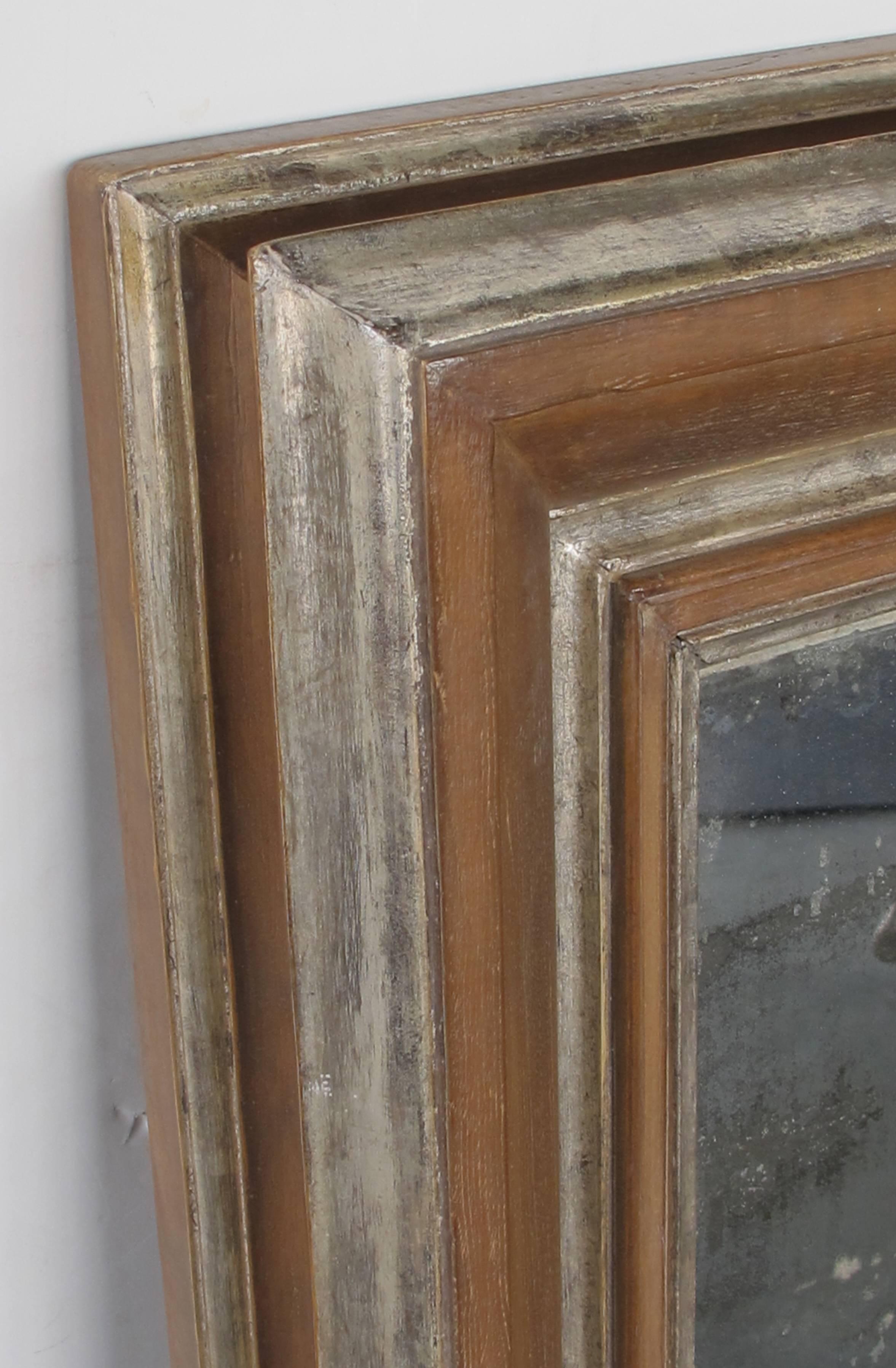 Der dicke und robuste Buchenholzrahmen mit silber-vergoldeten Akzenten umgibt die originale, antikisierte Spiegelplatte.