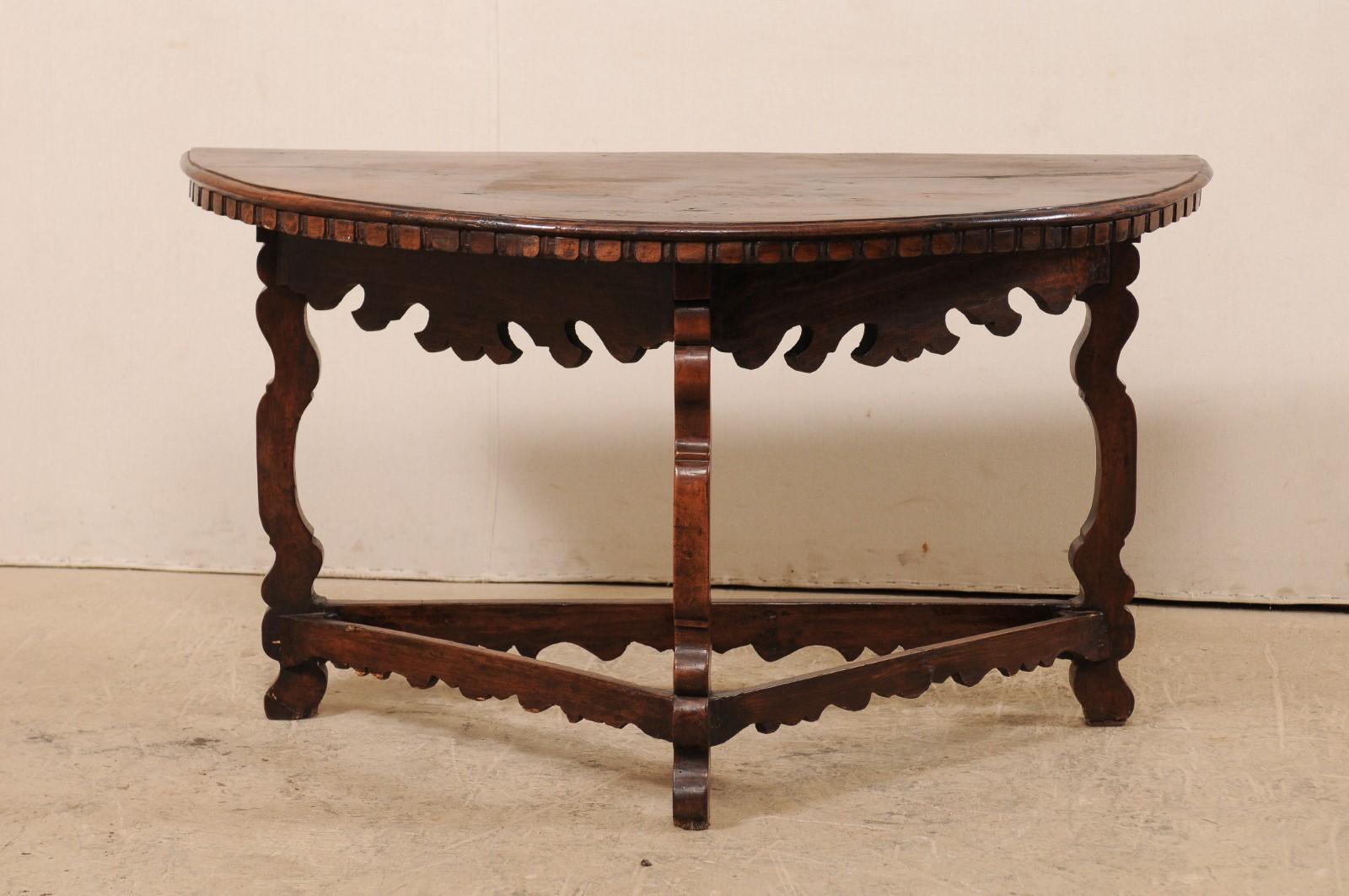 An 18th century Italian carved walnut wood demilune table. This antique demilune table from Italy of walnut wood features a half-moon shaped top accented in carved dentil trim just beneath the lip edge, an attractive and heavily carved
