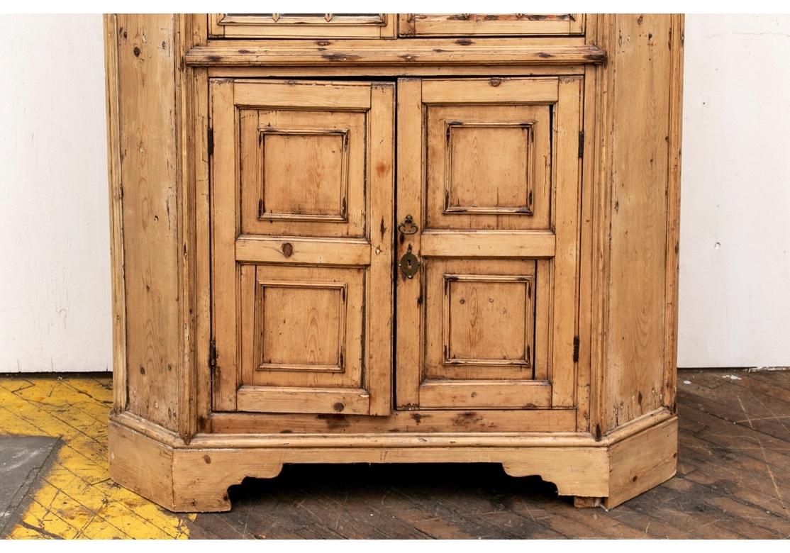 A large and handsome Stripped Pine Corner Hutch presumed English. A rustic constructed pine cabinet with a carved cornice over a dentil frieze. Double upper mullion doors with a turn lock opening to two shaped shelves. Double paneled lower doors