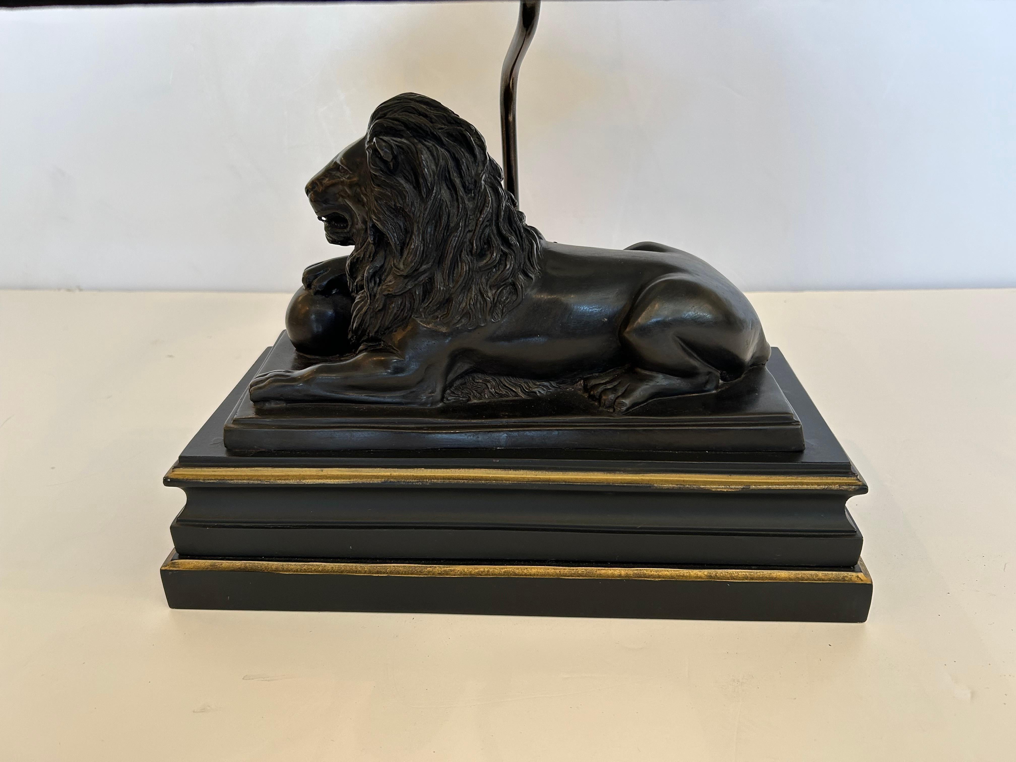 Impressive large black and gold table lamp having reclining lion sculpture on stepped base and elegantly shaped black lamp shade.