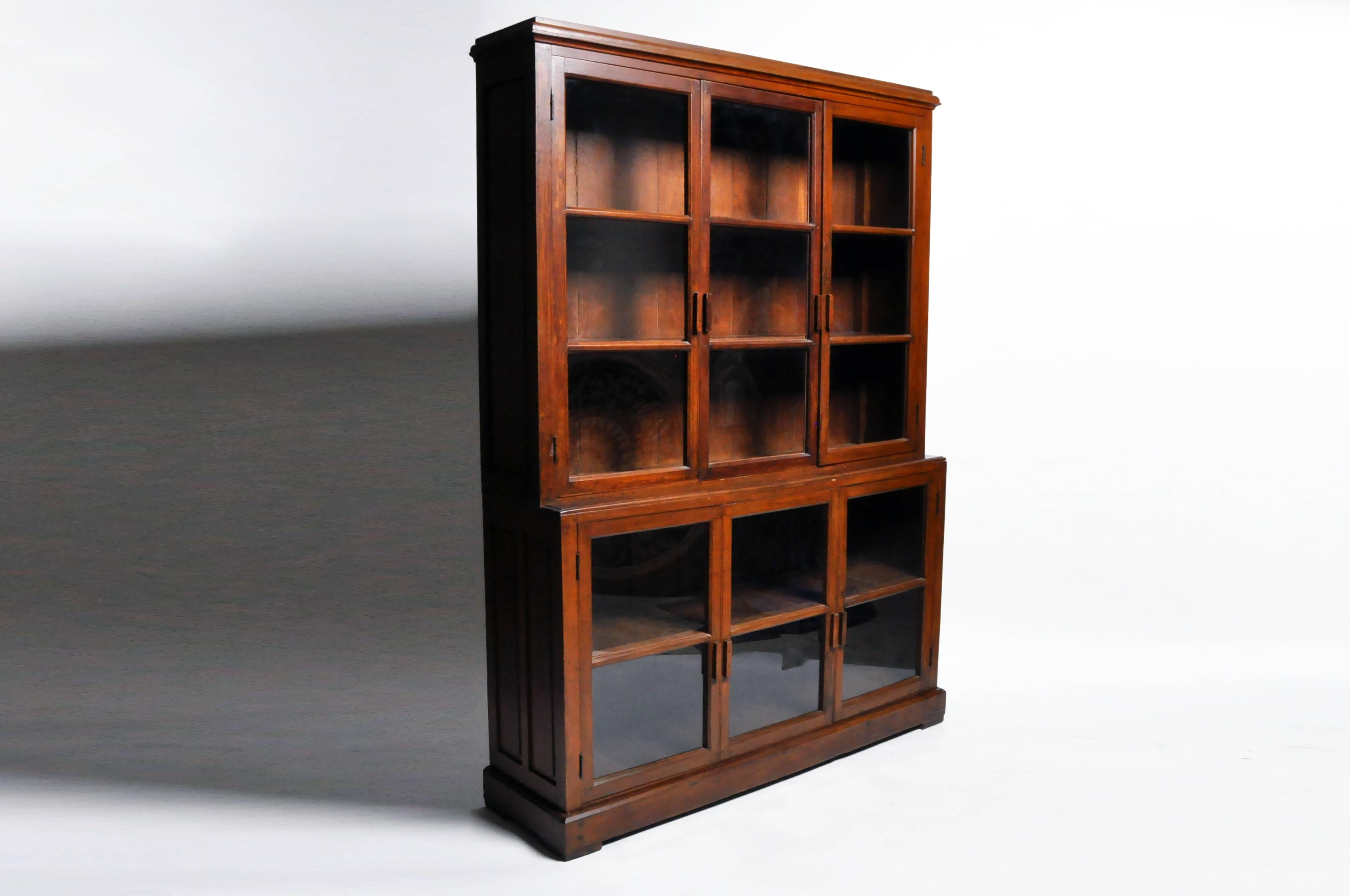 This British Colonial breakfront bookcase comes in two parts; both the top and bottom have two pairs of glass panel doors and one sliding door that opens up to compartments lined with shelves. It's scale and ample storage make this a perfect book