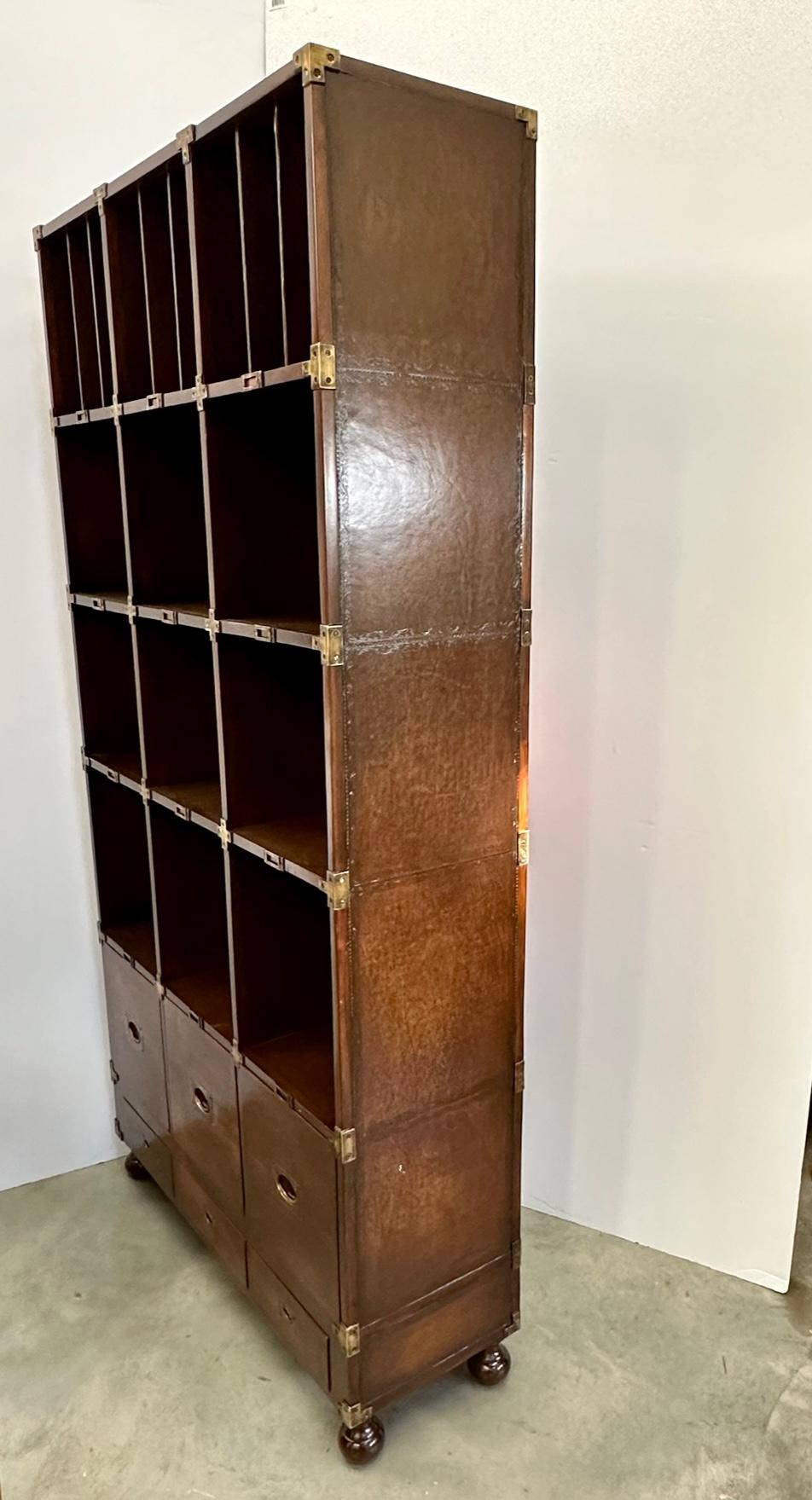 Stunning large leather wrapped bookcase attributed to Theodore Alexander having his signature embossed leather decoration on the sides. Super functional for display and storage having 6 drawers at the bottom and 9 cubbies that are 12