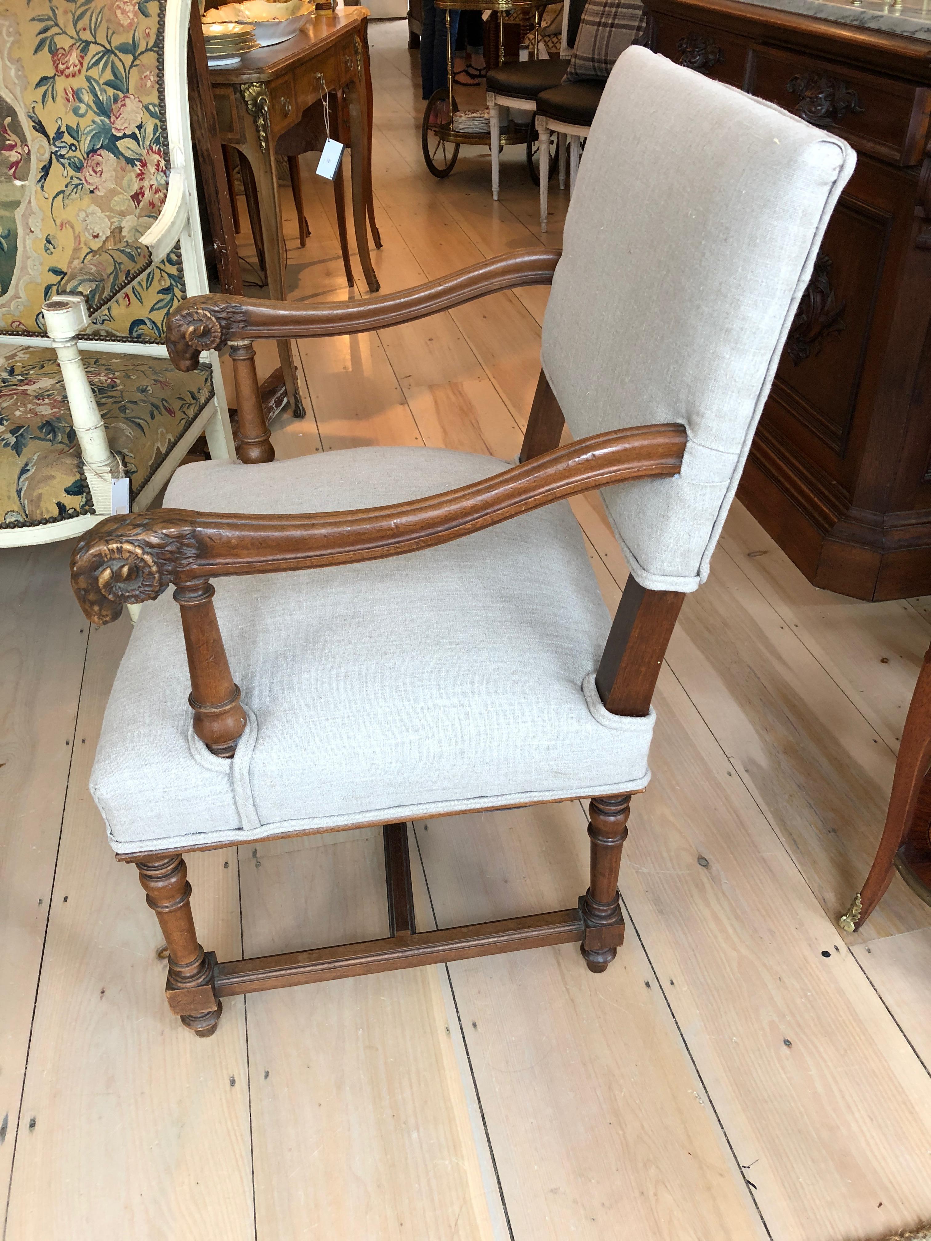 A sophisticated beige linen upholstered antique French armchair having handsome carved walnut arms with fabulous rams heads at the ends, and beautiful stretcher underneath.
Measures: Arm height 25; seat depth 22.