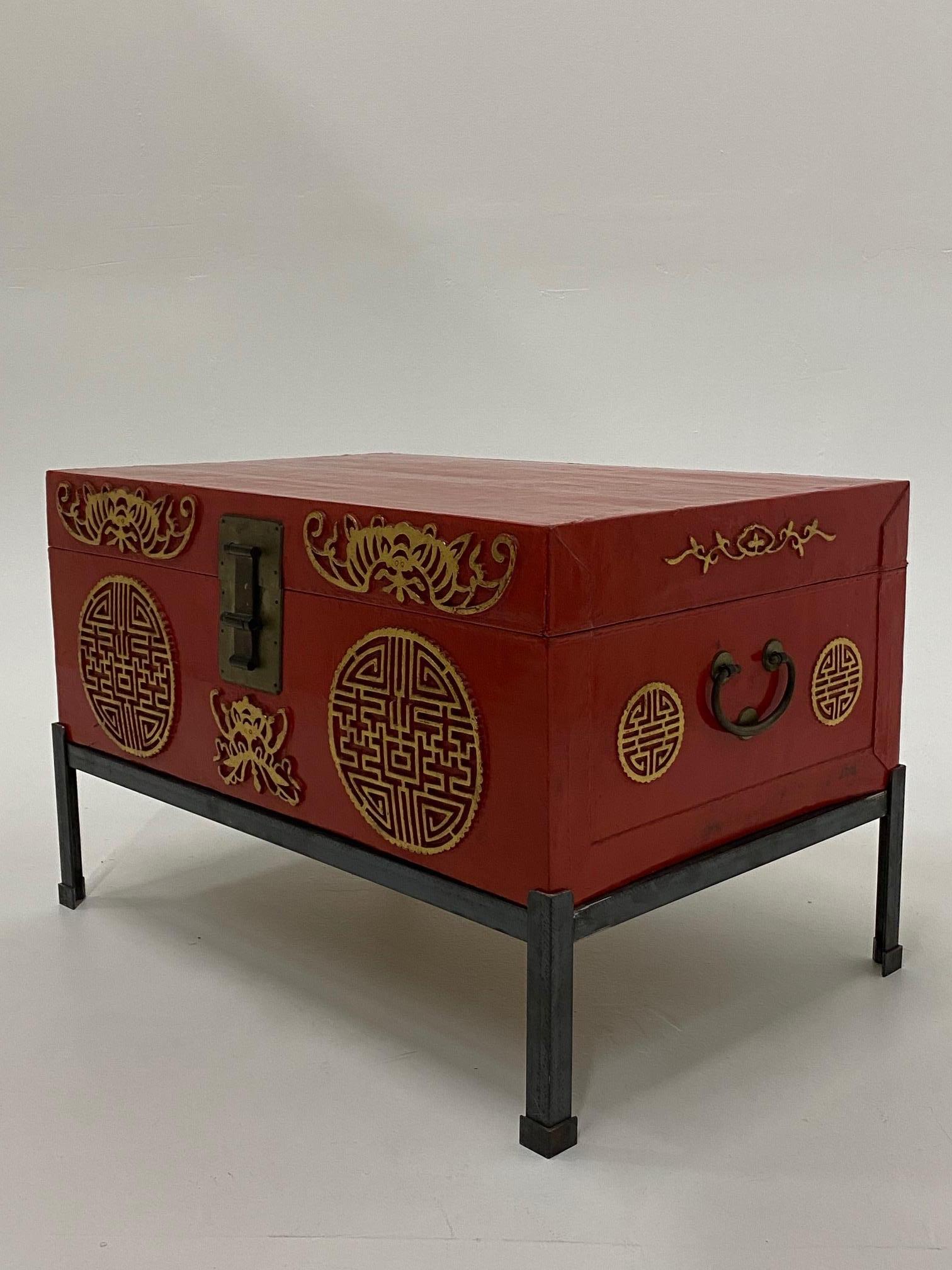 Wonderful Chinese red trunk with raised gold medallions that rests on a custom iron stand.