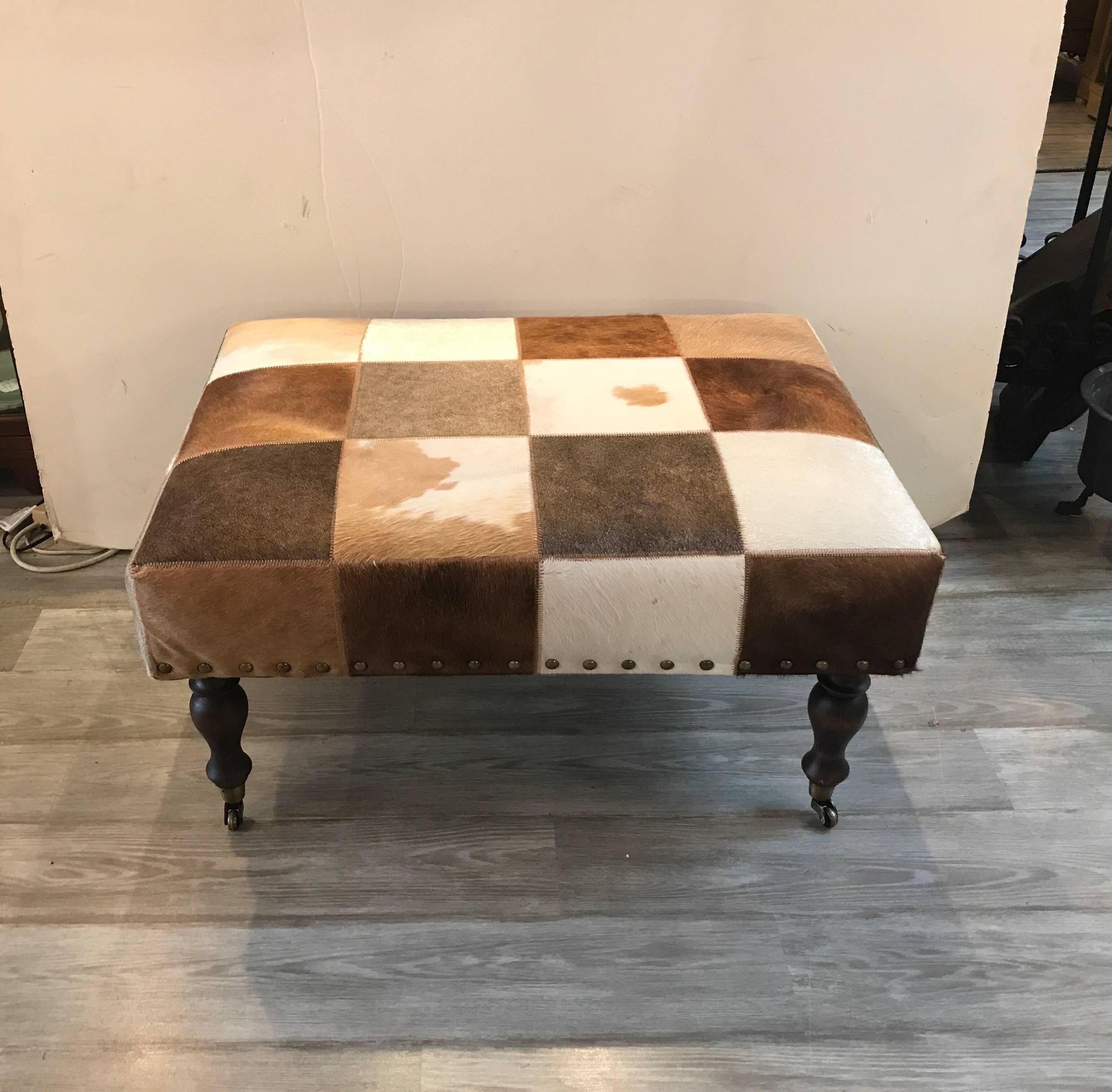 A natural cowhide rectangular ottoman with dark hardwood turned legs and brass castors. Perfect for an alternative to a cocktail table.