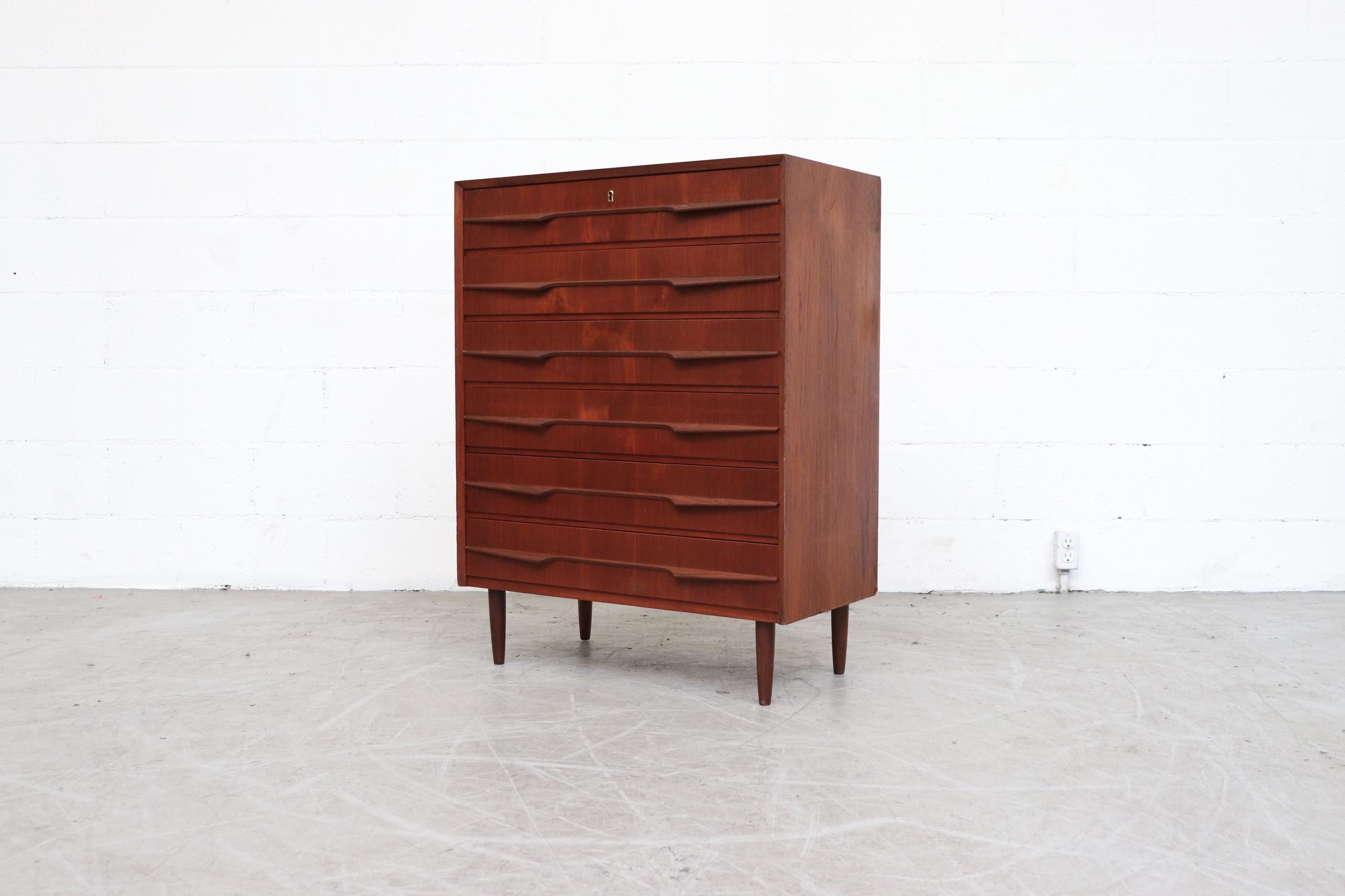 Tall Danish midcentury teak dresser. 6 drawers with organically wing-like carved hand pulls and tapered legs. Fluid grain pattern throughout the drawers. Lightly refinished. In good original condition with some signs of wear consistent with age and
