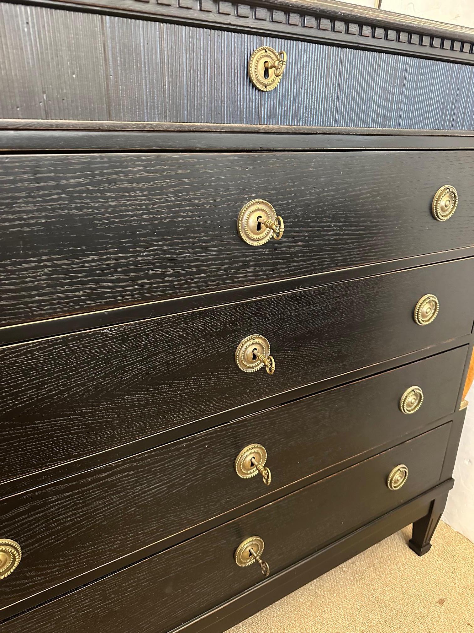 
Black ebonized handsome Regency style dresser having 5 drawers, each with key.  Beautiful decoration includes honey colored wood columns with gilded tops flanking the sides of the chest.