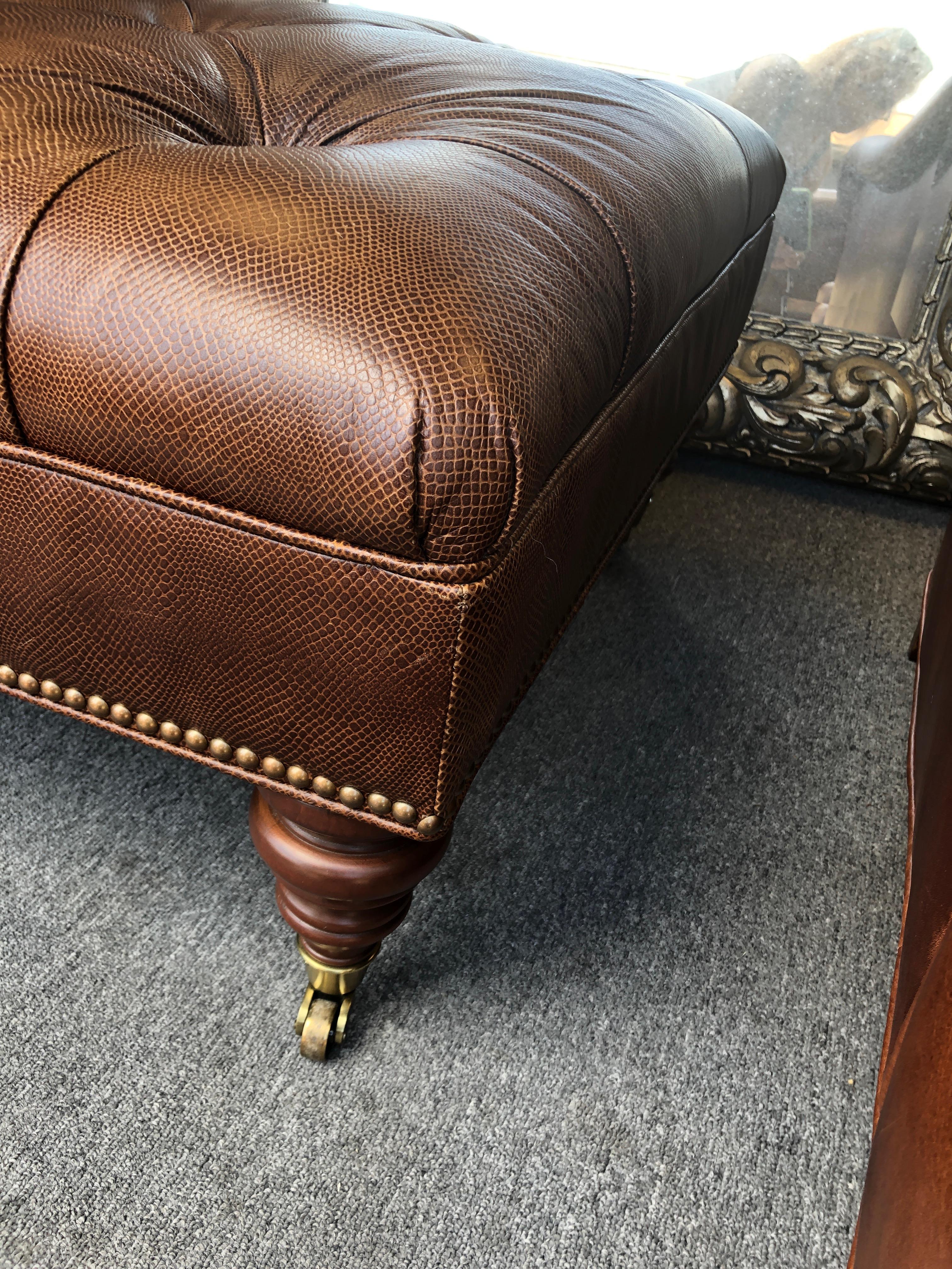 Great looking embossed leather tufted ottoman that looks like small pattern crocodile, having wooden turned feet on brass casters and nailhead detailing.