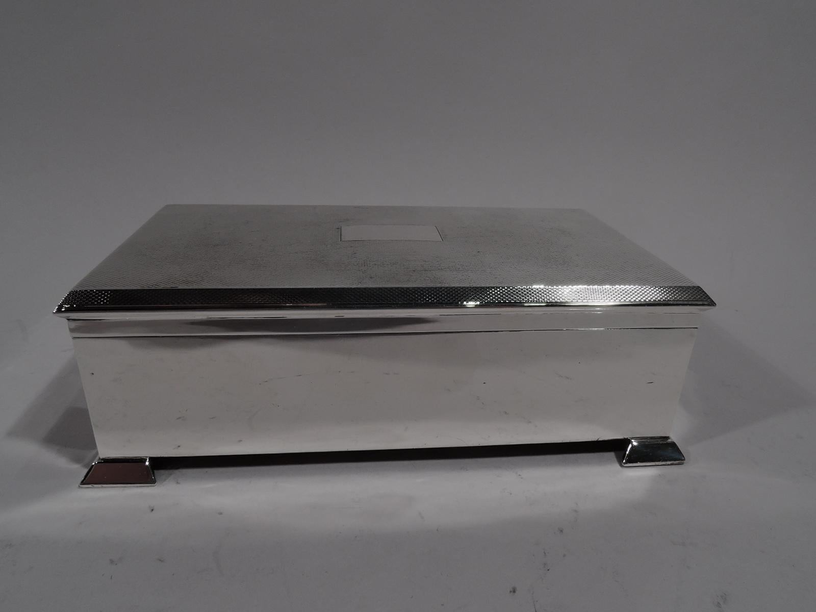 Handsome Art Deco sterling silver box. Made by Stephen Julian Rose & Son in London in 1957. Rectangular with plain straight sides and corner bracket supports. Cover hinged with canted rim and all-over engine turning as well as plain central mono