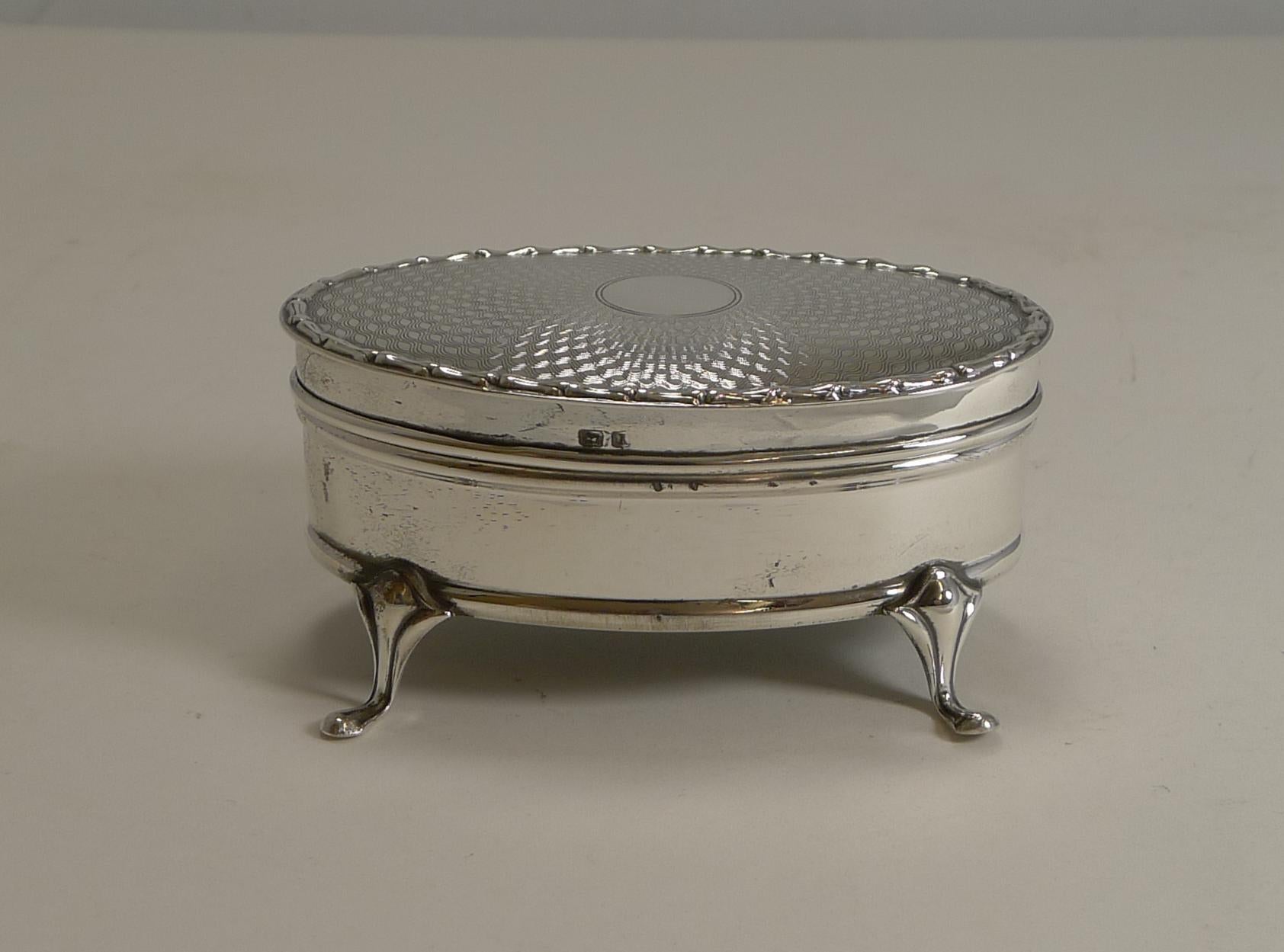 A fabulous sterling silver jewelry box standing on four very elegant feet with a stunning engine-turned decorated lid surrounding a central circular vacant cartouche.

The hinged lid fits well and has a lovely raised border. The lid opens to