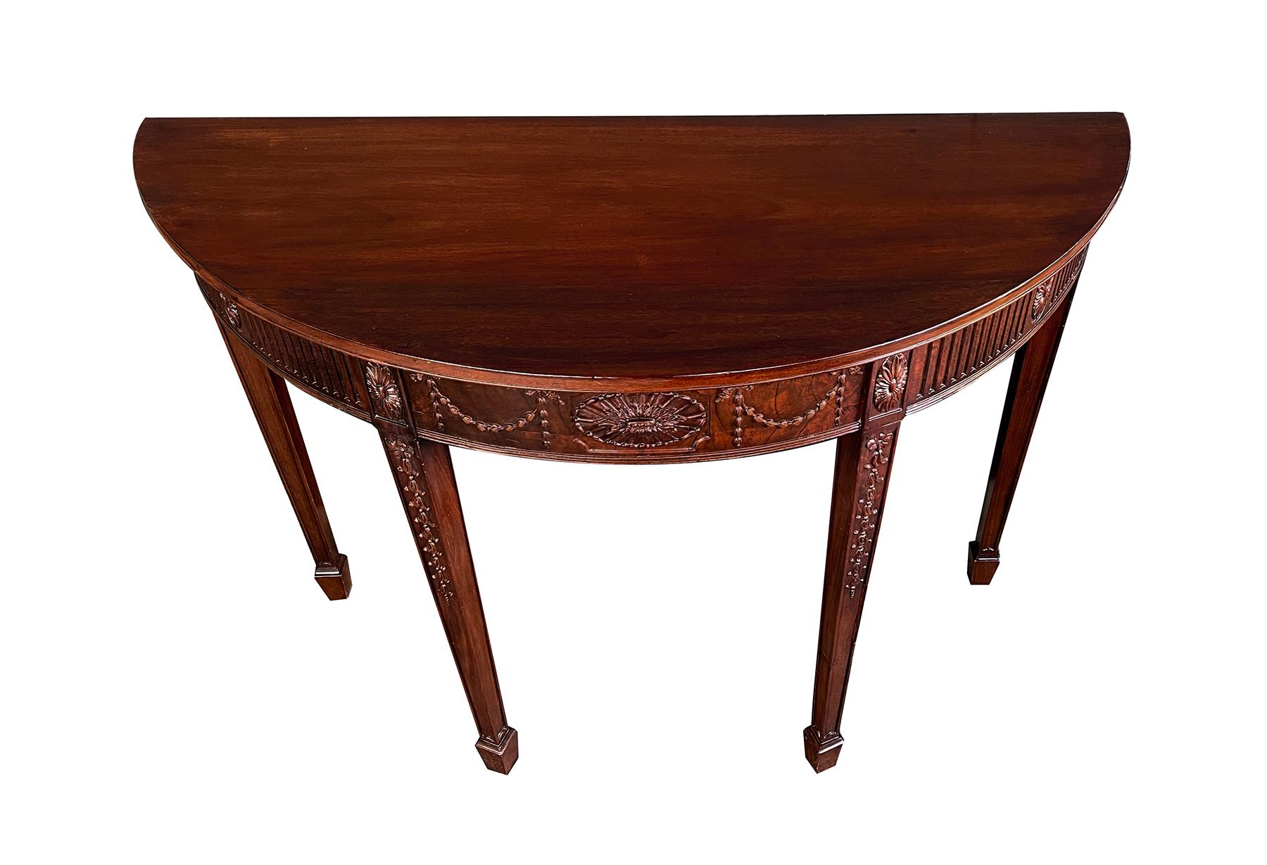 the half-round top above a conforming apron centering a foliate reserve flanked by swag festoons and carved paterae with fluted panels; all raised on tapering quadrangular supports adorned with cascading bell-flowers all ending in a spade foot