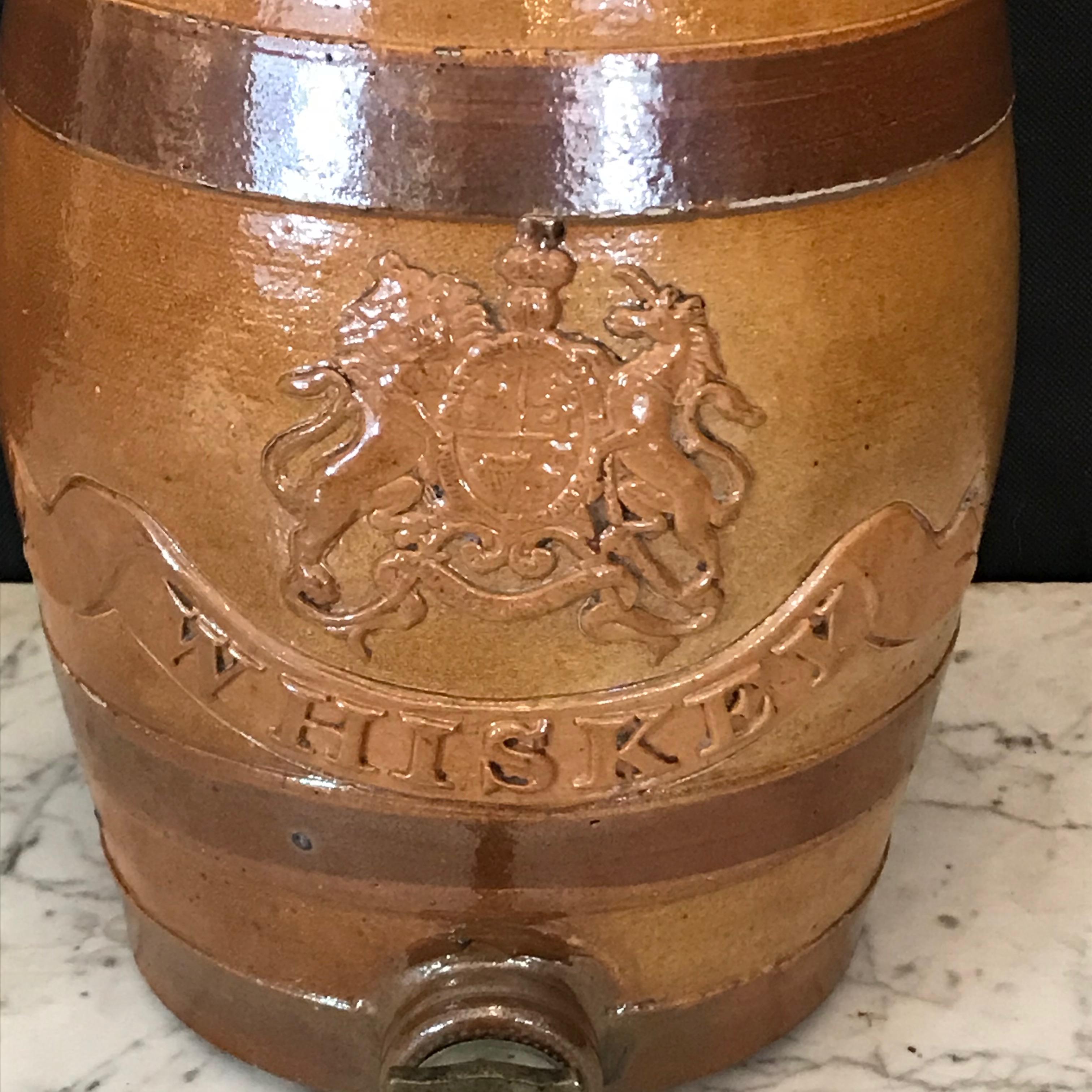An English stoneware spirit barrel from the mid-19th century. The glazed body is shaped like a barrel decorated with low-reliefs depicting the United Kingdom’s royal coat of arms, complete with a lion on the left and a unicorn on the right. Above