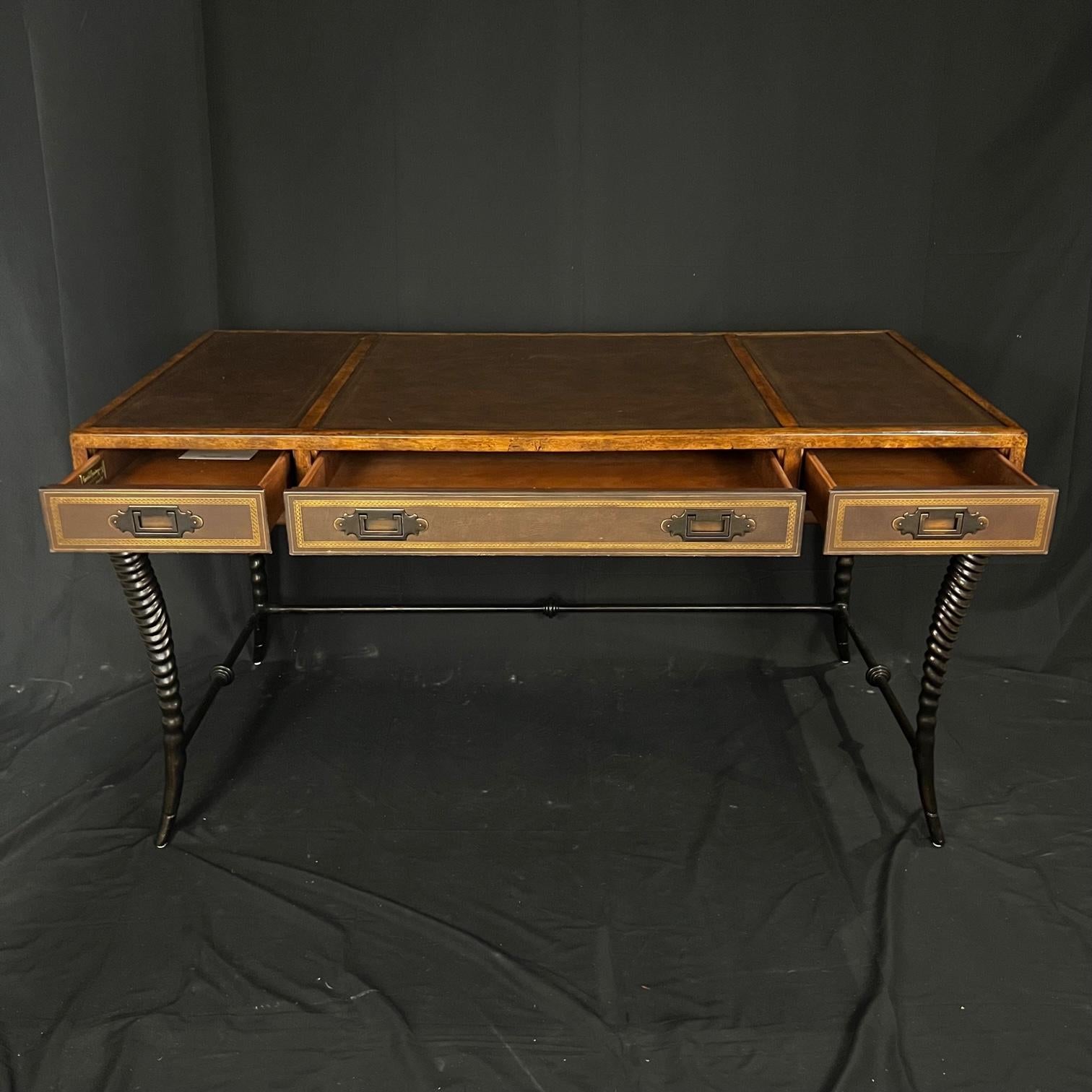A dramatic campaign style desk having walnut of a golden brown color, with stunning twisted metal curved legs resembling the tusks of exotic animals. The table top and drawer fronts are trimmed with rich brown tooled embossed leather with carved