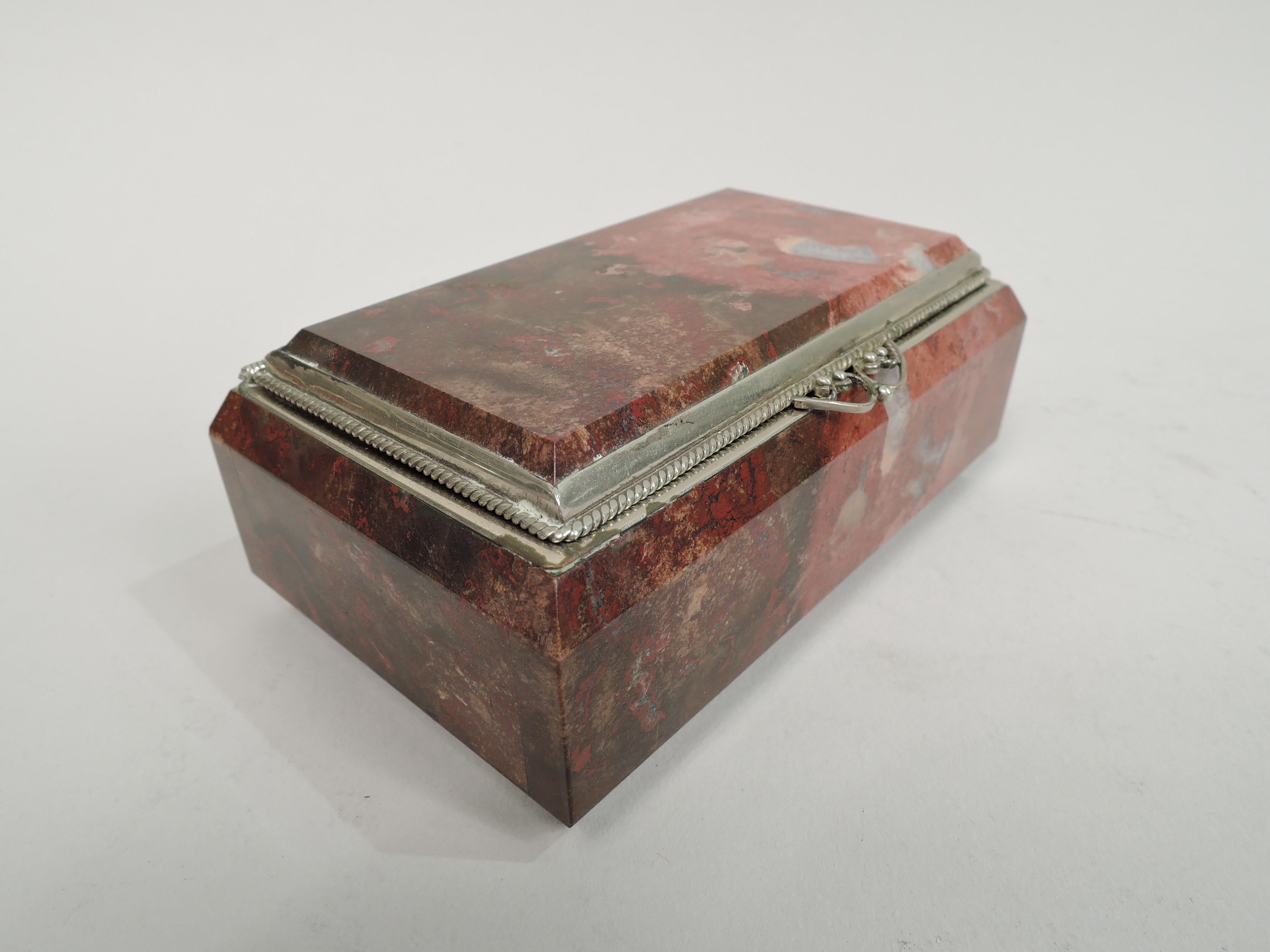 Handsome European stone trinket box, ca 1910. Rectangular with straight sides and sharp corners. Shoulder and base chamfered. Cover hinged, inset, and chamfered. Silver-plated mouth and cover rims. Cover has cabled border and filigree scrolled tab.