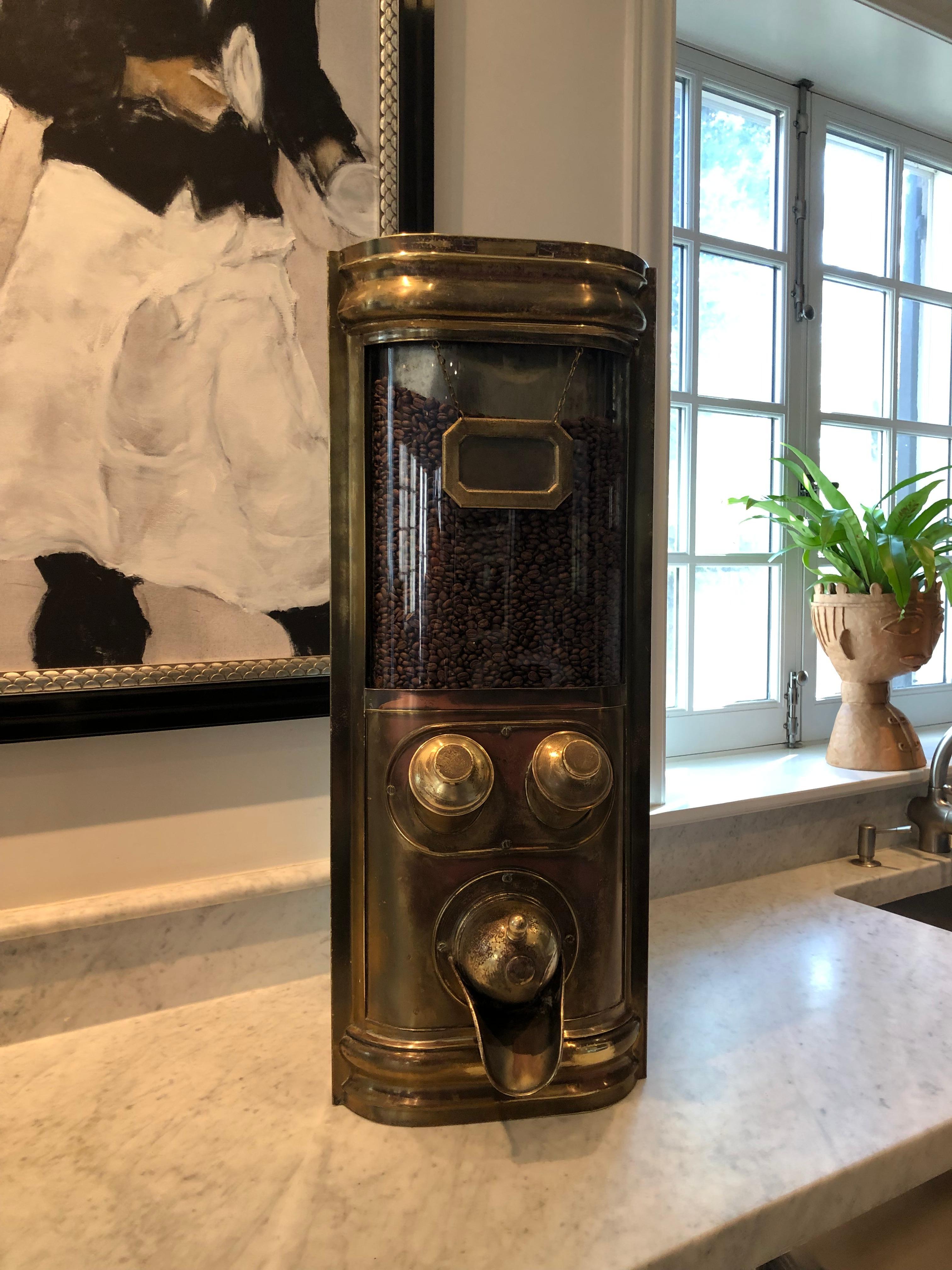 Striking commercial coffee bean dispenser in brass. The dispenser allows you to dispense the desired measure of beans or to use one of the two scoops that are housed in the custom-fitted mounts. The brass has been polished by hand; a professional