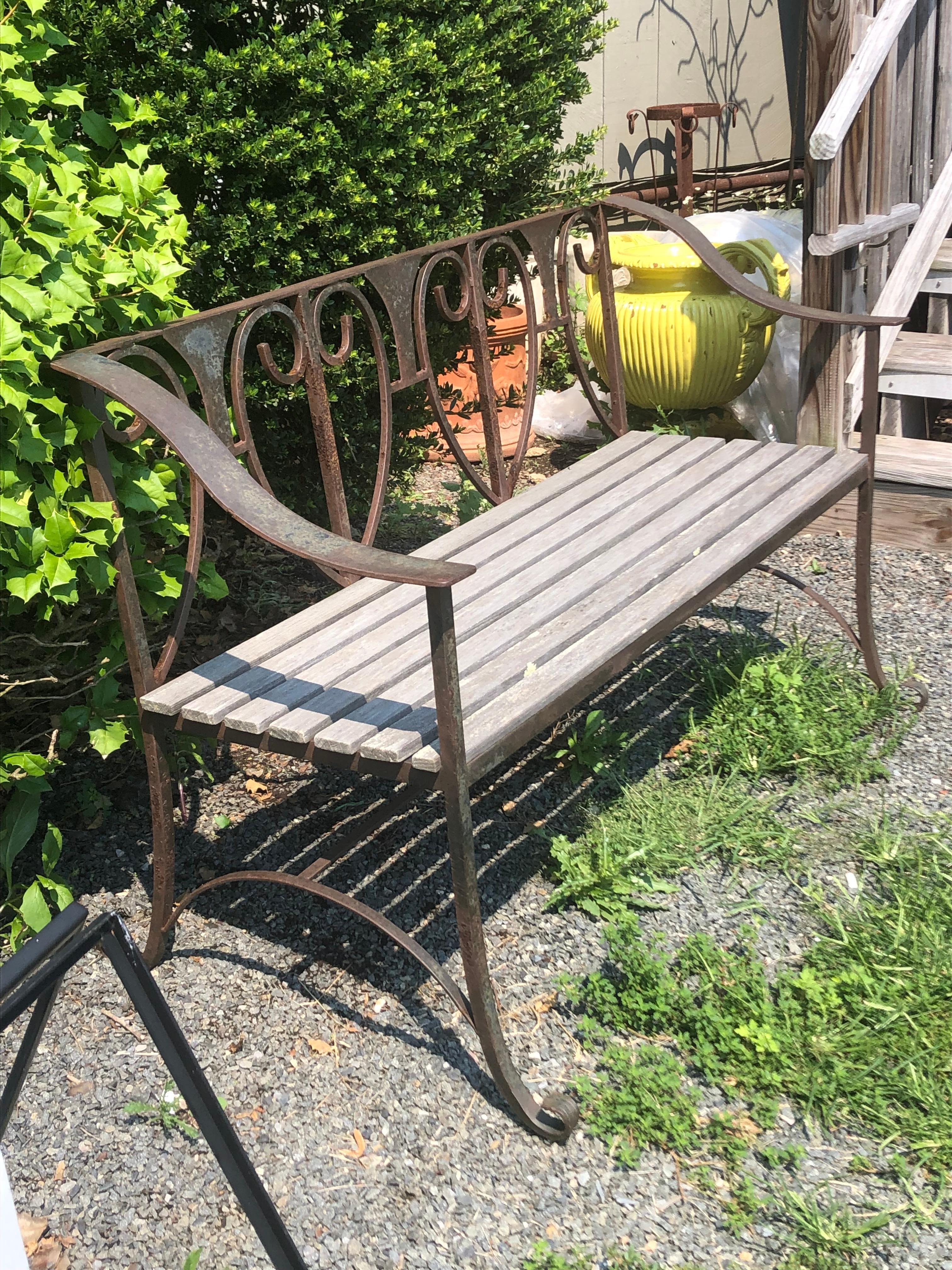 A great looking vintage outdoor bench having weathered hand forged iron with heartshaped curlicue back, curved arms and feet, and wooden slat seat. 
seat depth 18
arm height 26