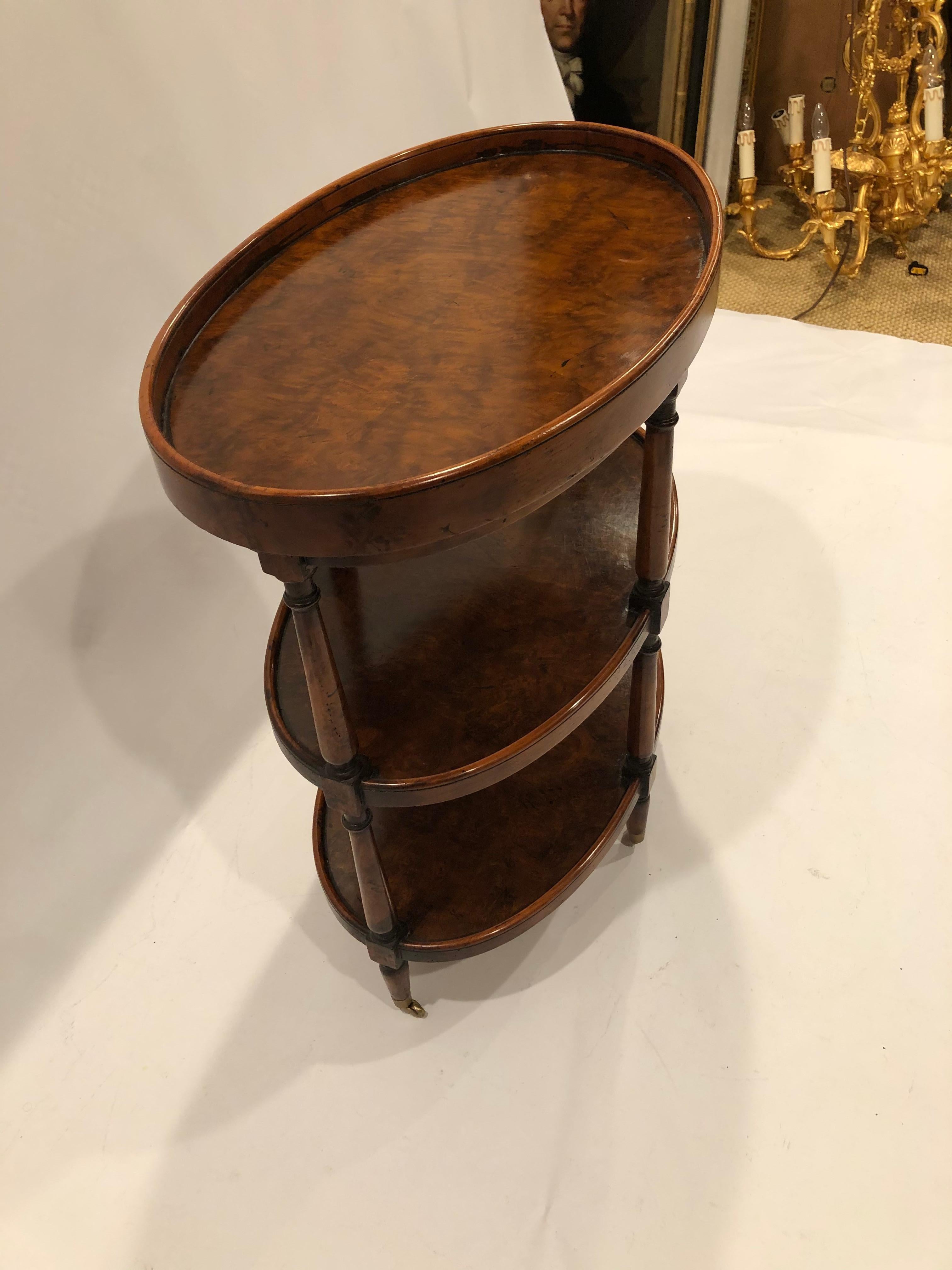 Handsome very versatile oval 3 tier side table with beautiful bookmatched burl wood and brass casters.