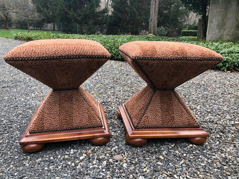 Handsome pair of ottomans by Baker upholstered in a brown and camel animal print. The ottomans have cinched waists and are decorated throughout in antiqued brass nail head trim. Each ottoman rests upon mahogany frames that sit on bun feet. These are