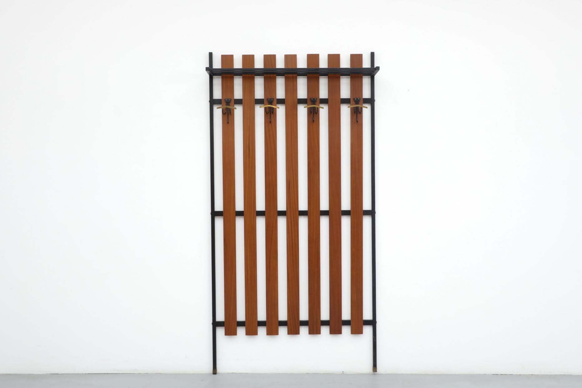 Large Italian Gianfranco Frattini style wall mounted vertically slatted teak coat rack with 4 brass accented hooks on a black enameled metal frame. This elegant entry piece also has a black metal hat rack. In original condition with some wear