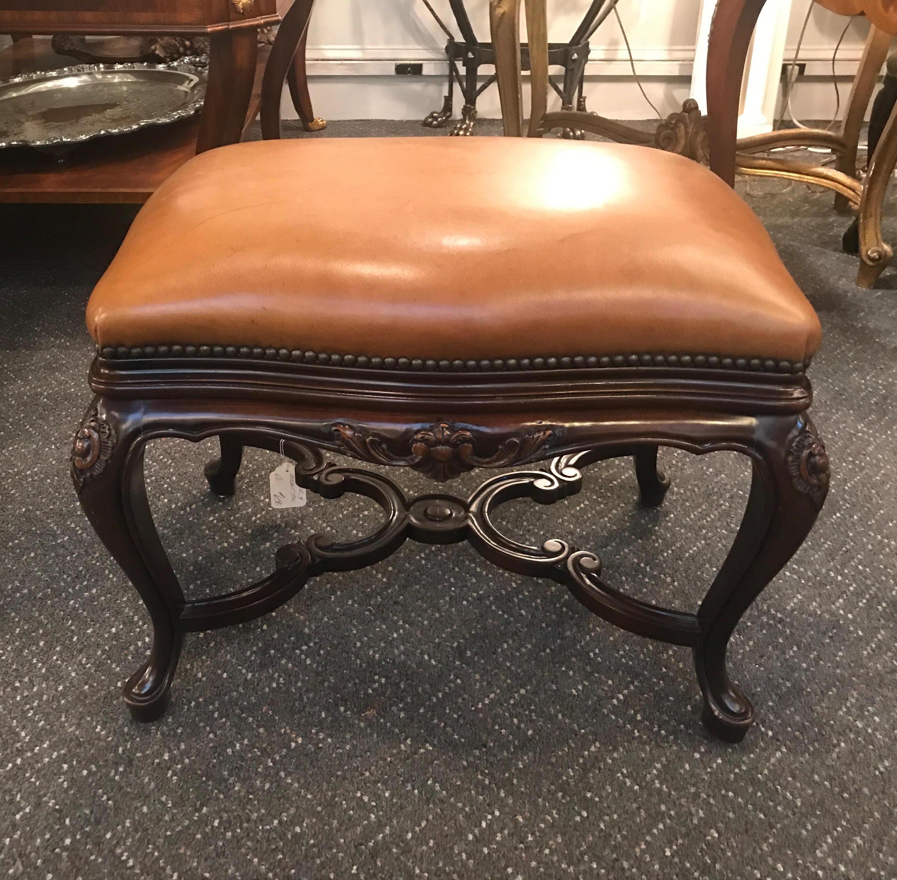 A deep brown walnut base with nicely carved details with camel color leather seat and aged nailhead trim. The carved legs with cabriole shape with a nicely detailed stretcher base. There are some natural variations in the leather.   
  