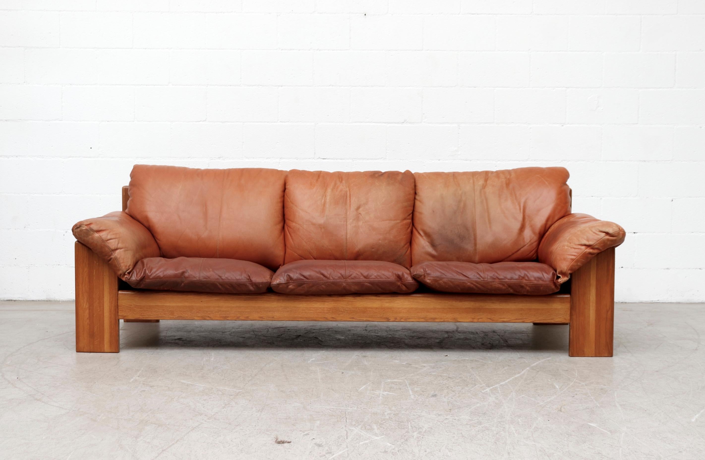 Handsome Leolux 3-seat with thick well worn cognac leather and lightly refinished oak frame with matching leather inset panel in the back. Cushions show visible wear with discoloration and some staining. Heavy patina. Sofa frame in good original