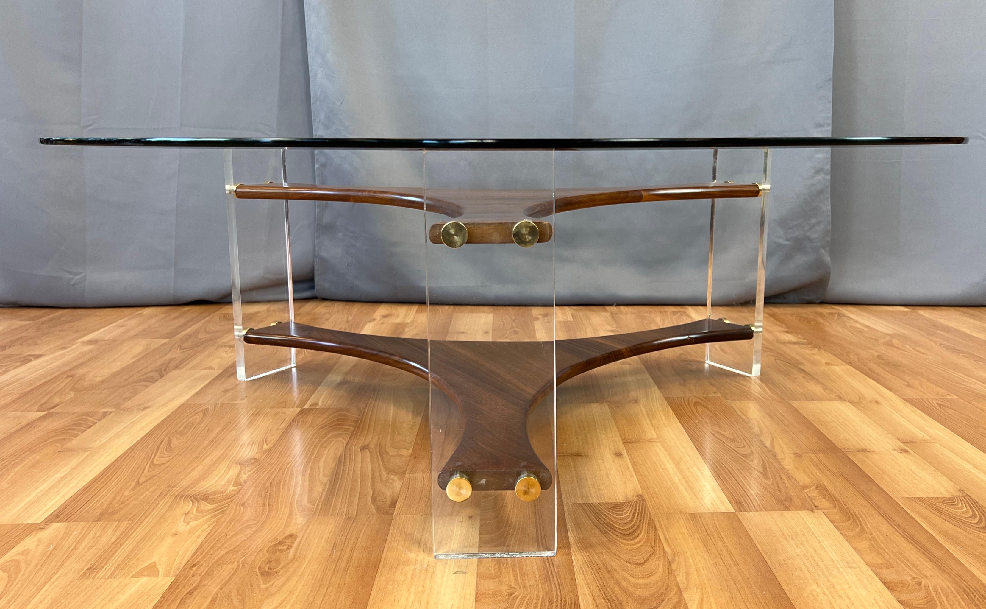 Offered here is a very handsome round beveled glass coffee table. With rectangular lucite legs connected to each other by a 
sculptural Walnut frame. With each lucite leg held onto the Walnut with four brass knobs.
With no markings, but such nice