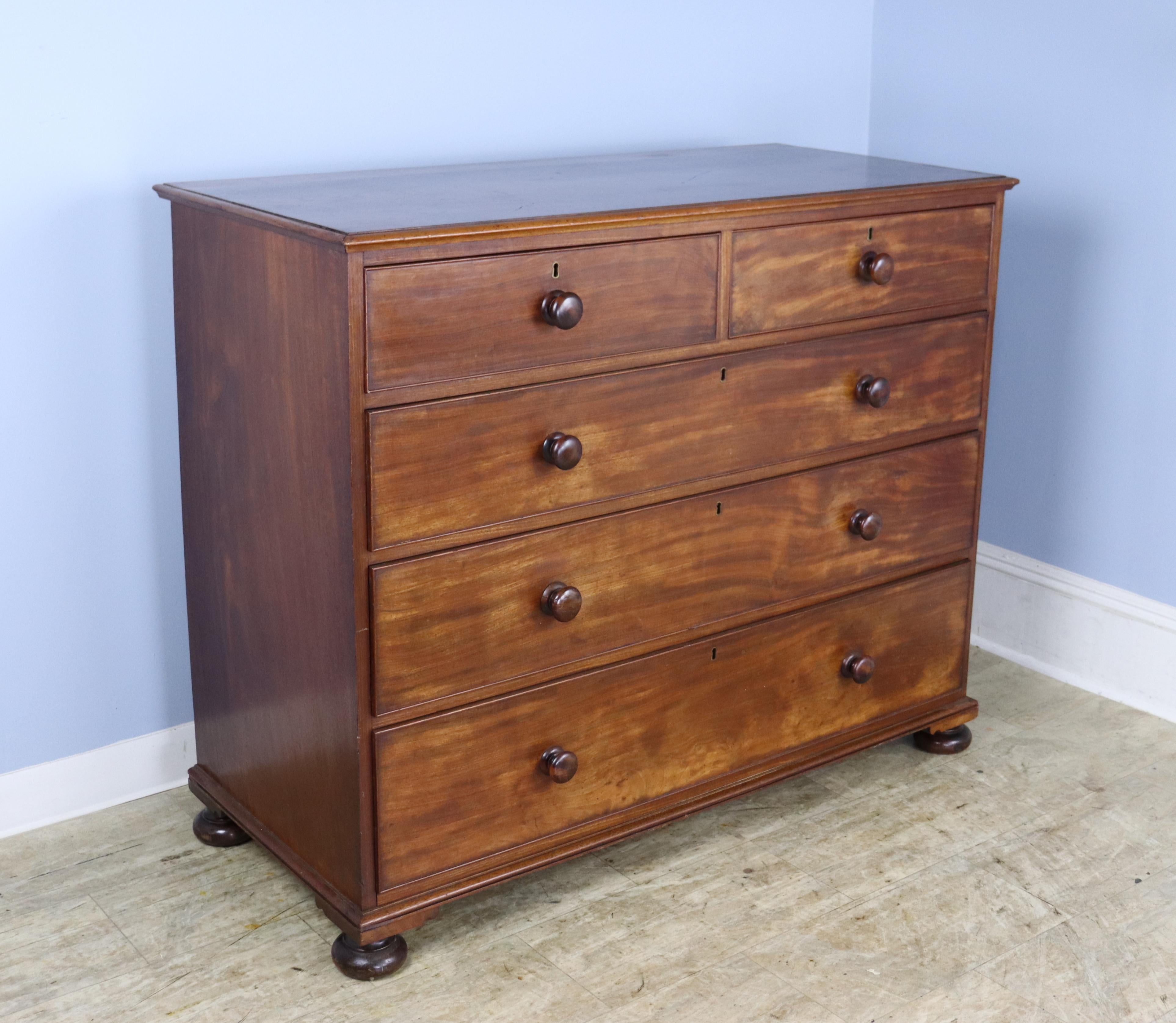 A large chest of drawers in rich mahogany, with very deep drawers and stylish glossy knobs.  Sweet bun feet complete the look.  The brass keyholes are original although there are no keys.  There is some light wear throughout the piece, mostly light