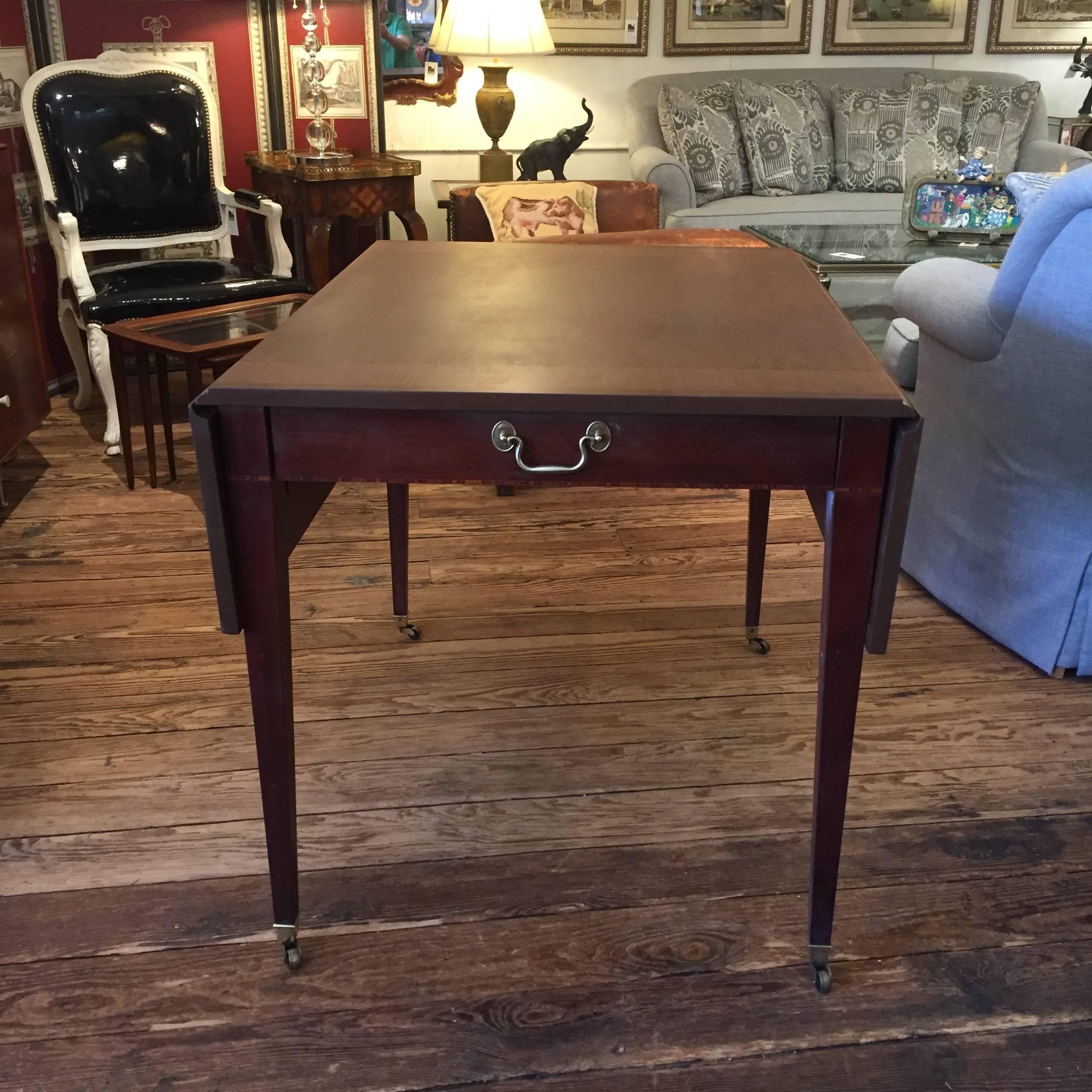 Very versatile traditional drop-leaf mahogany table having a single drawer, tapered legs on brass casters, and handsome inlay with different shades of wood. Label inside drawer.
Great behind a sofa, as a large side table, or a small dining table