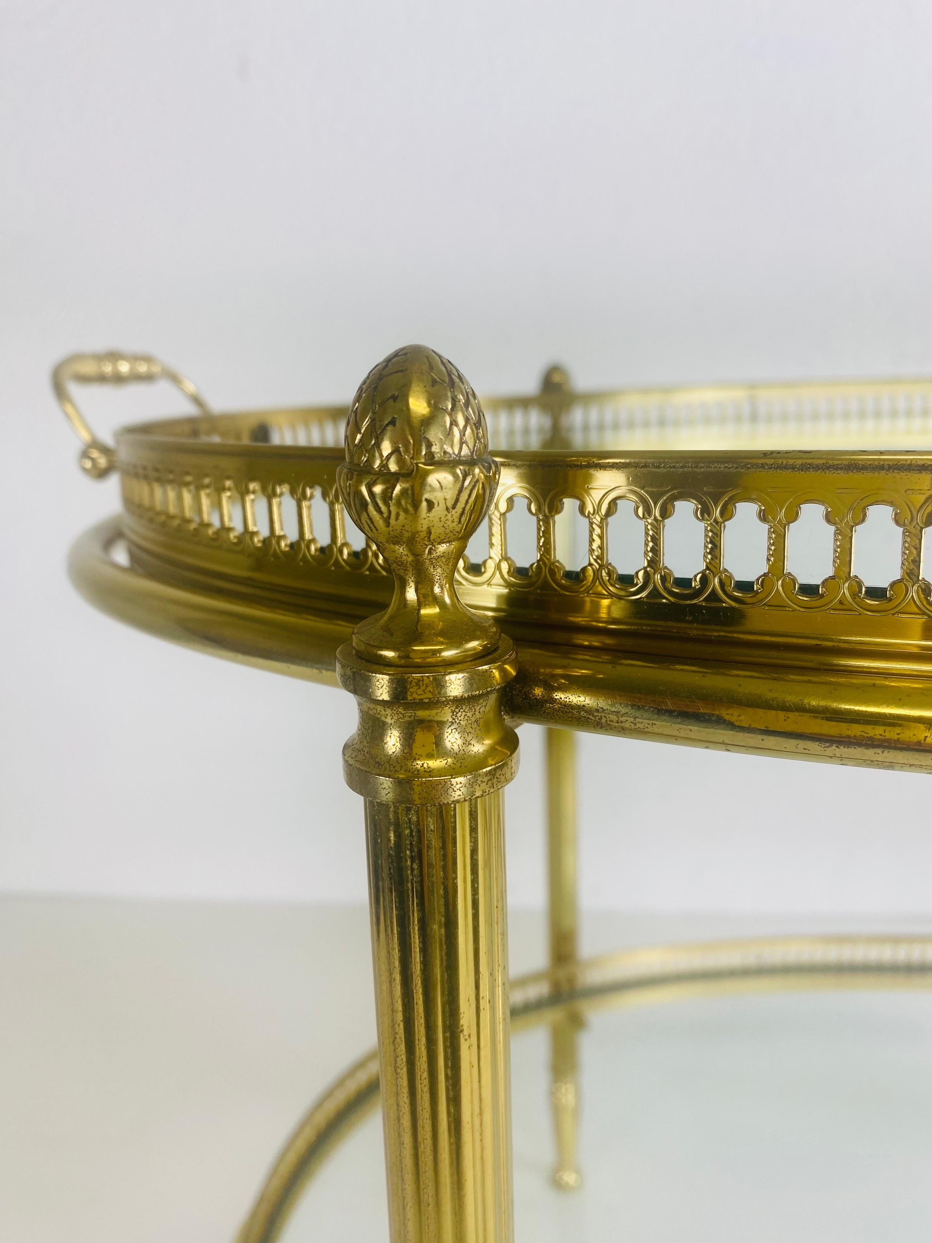 This is a solid brass side table that comes with two detachable gallery trays. The top tray has handles on either side as the lower tray does not. The table stands on four fluted legs with acorn finals at the top. The two trays have a beautiful
