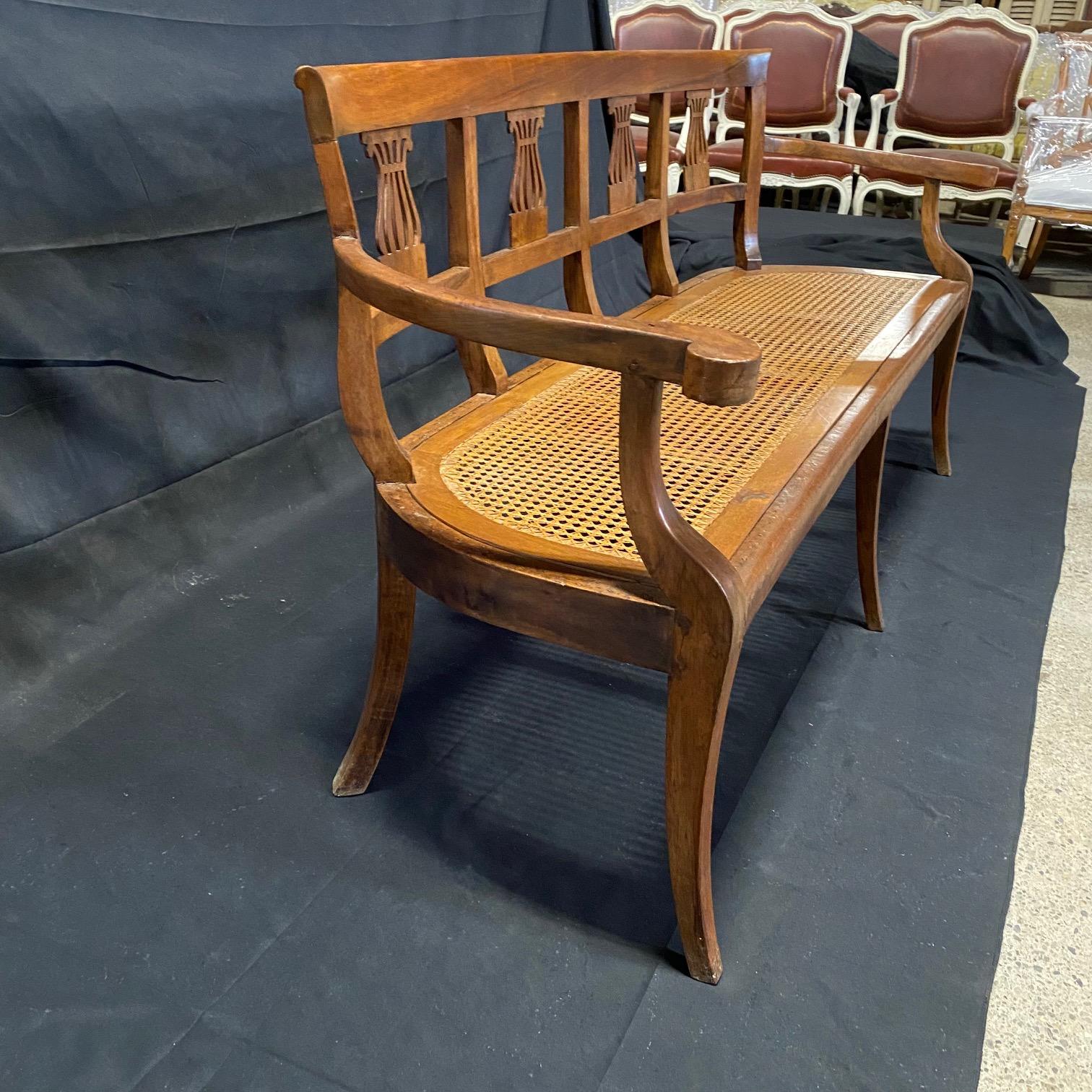 Exquisite mid century Italian neoclassical walnut sofa bench with hand carved back, tapered legs and immaculate caned seat. Lovely carved detail on the back depicting intricate urns, and on the gracefully tapered armrests. This sofa would make a