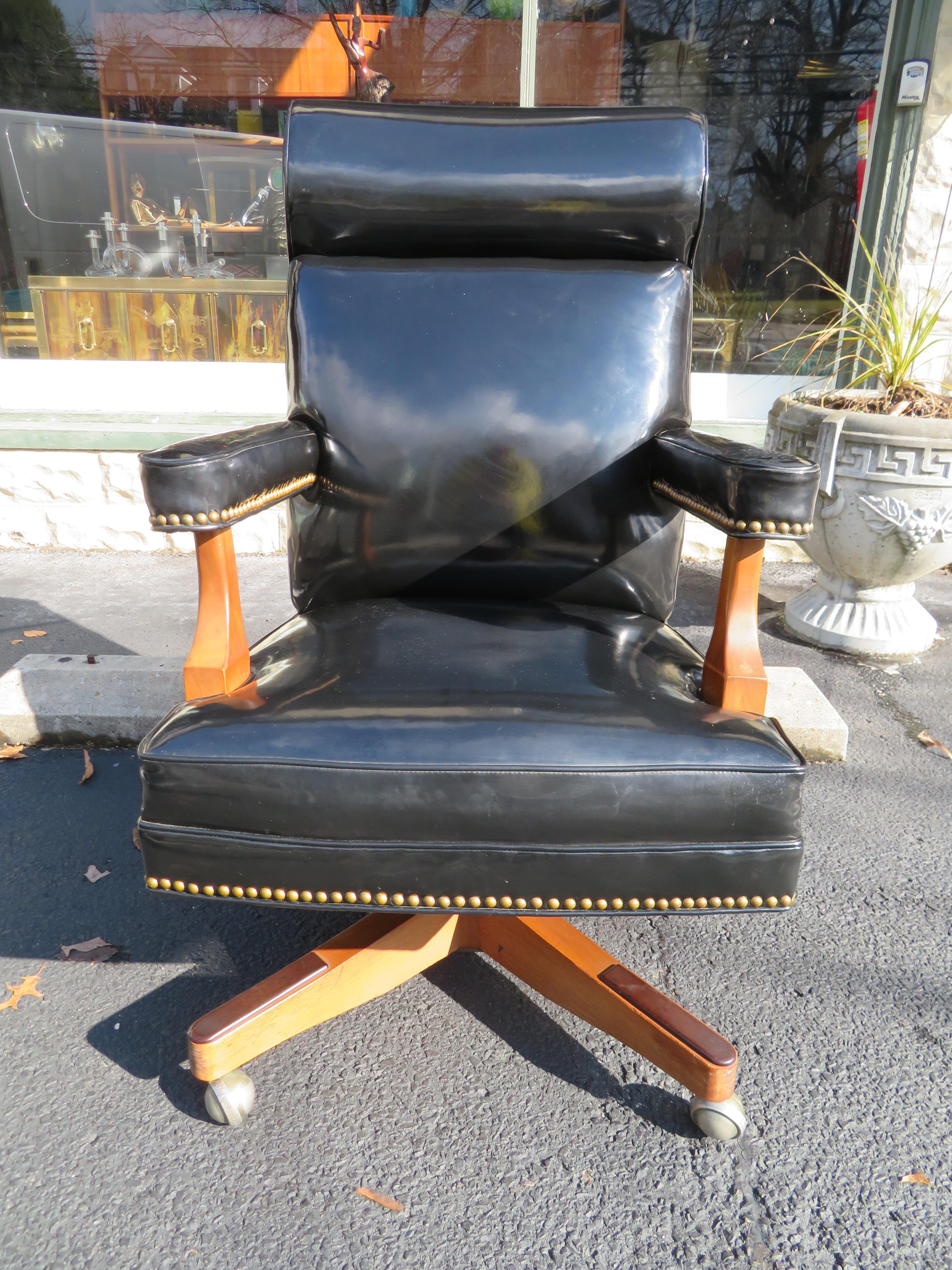 Handsome patent leather oversized rolling executive desk chair. This piece is stunning and impressive in person with its original black patent leather upholstery and brass nailhead details. And talk about comfortable this chair swivels and leans