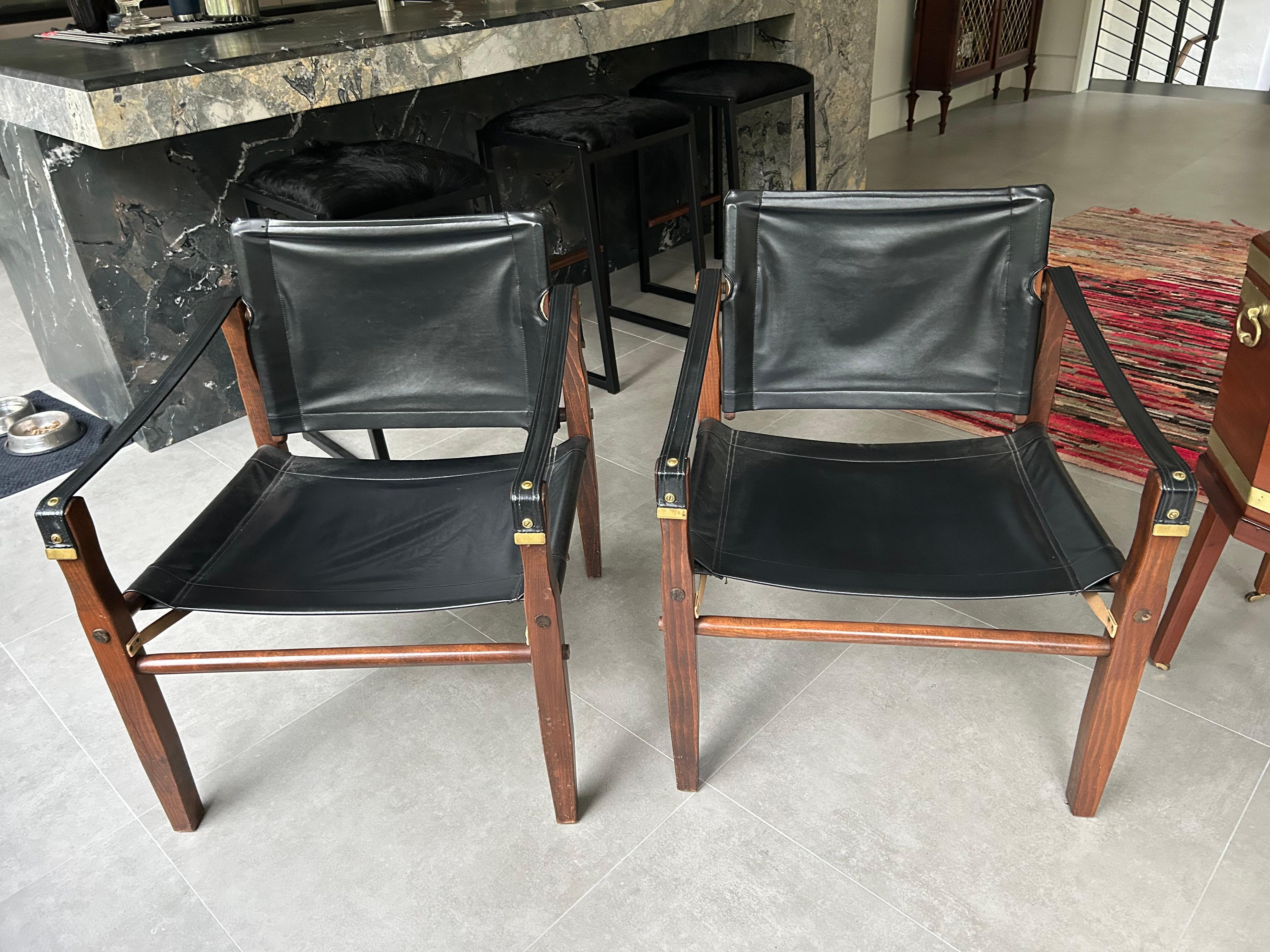 Handsome pair of safari style black leather or possibly vinyl club chairs by “Gold Medal” Foldiing Furniture Co. Racine Wisconsin.  Frames are warm wood and the grommets and straps are finished in brass.  Great looking chairs, light and easy to move.