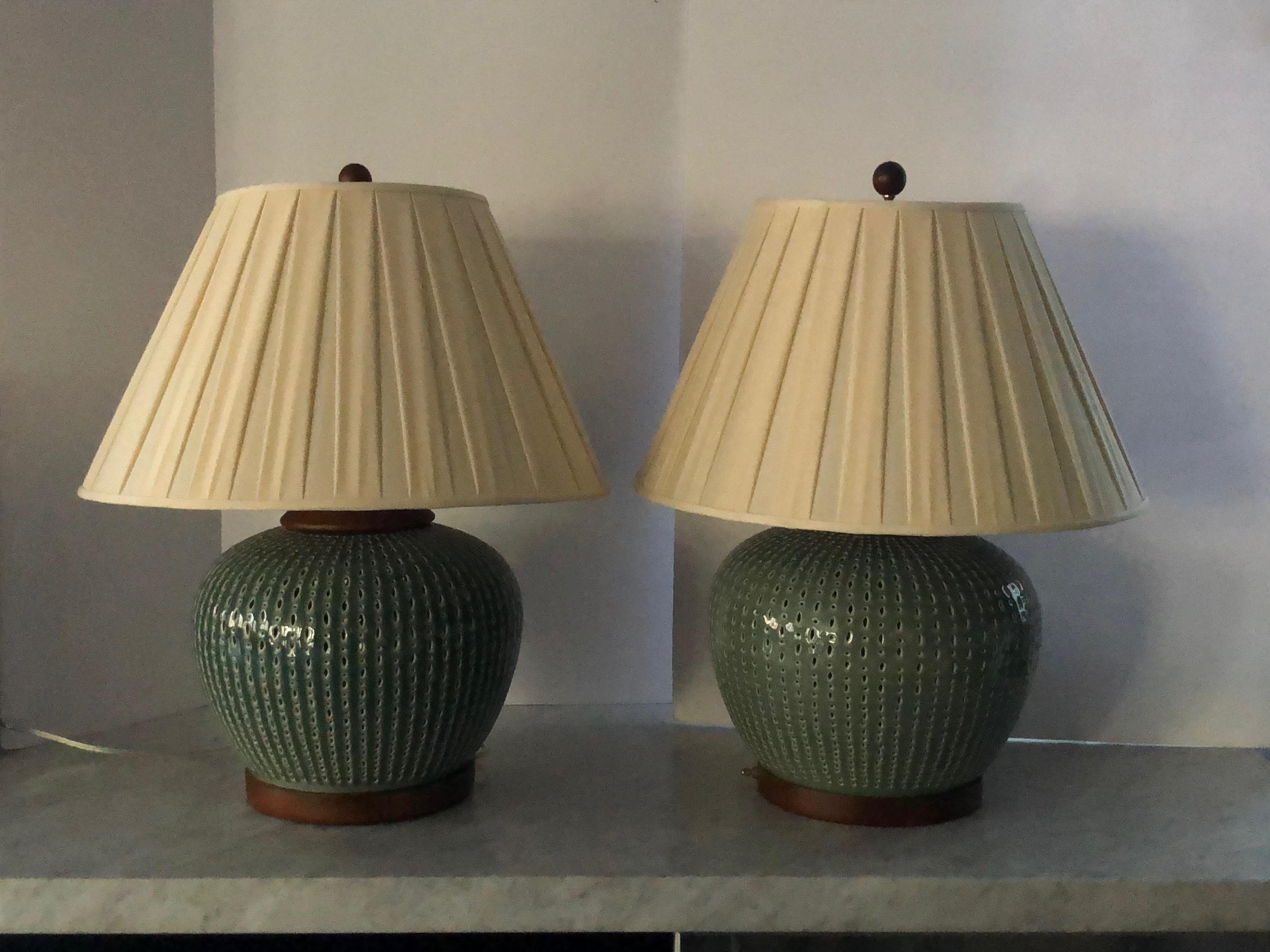 Fabulous pair of light teal blue ceramic lamps by Ralph Lauren. The ceramic body of each lamp is perforated, allowing light to show from within. This second interior bulb has a separate switch and should not exceed 40 watts. Wood trim, base and