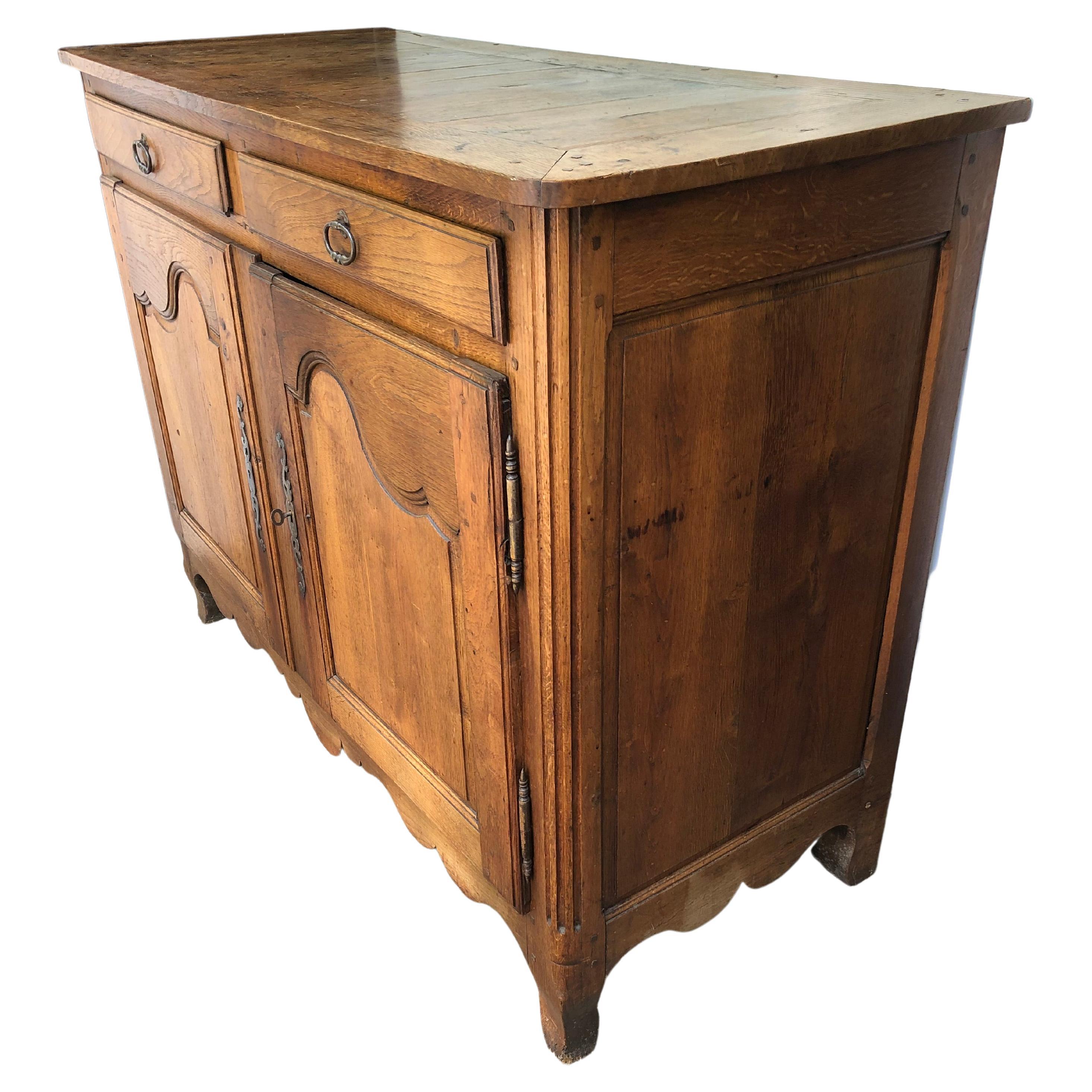 Rustic French Country oak sideboard or buffet having carved paneled two door front with two drawers above. Original hardware and wonderful aged slightly distressed patina. We love the wooden nailheads that are visible on top. Great storage inside