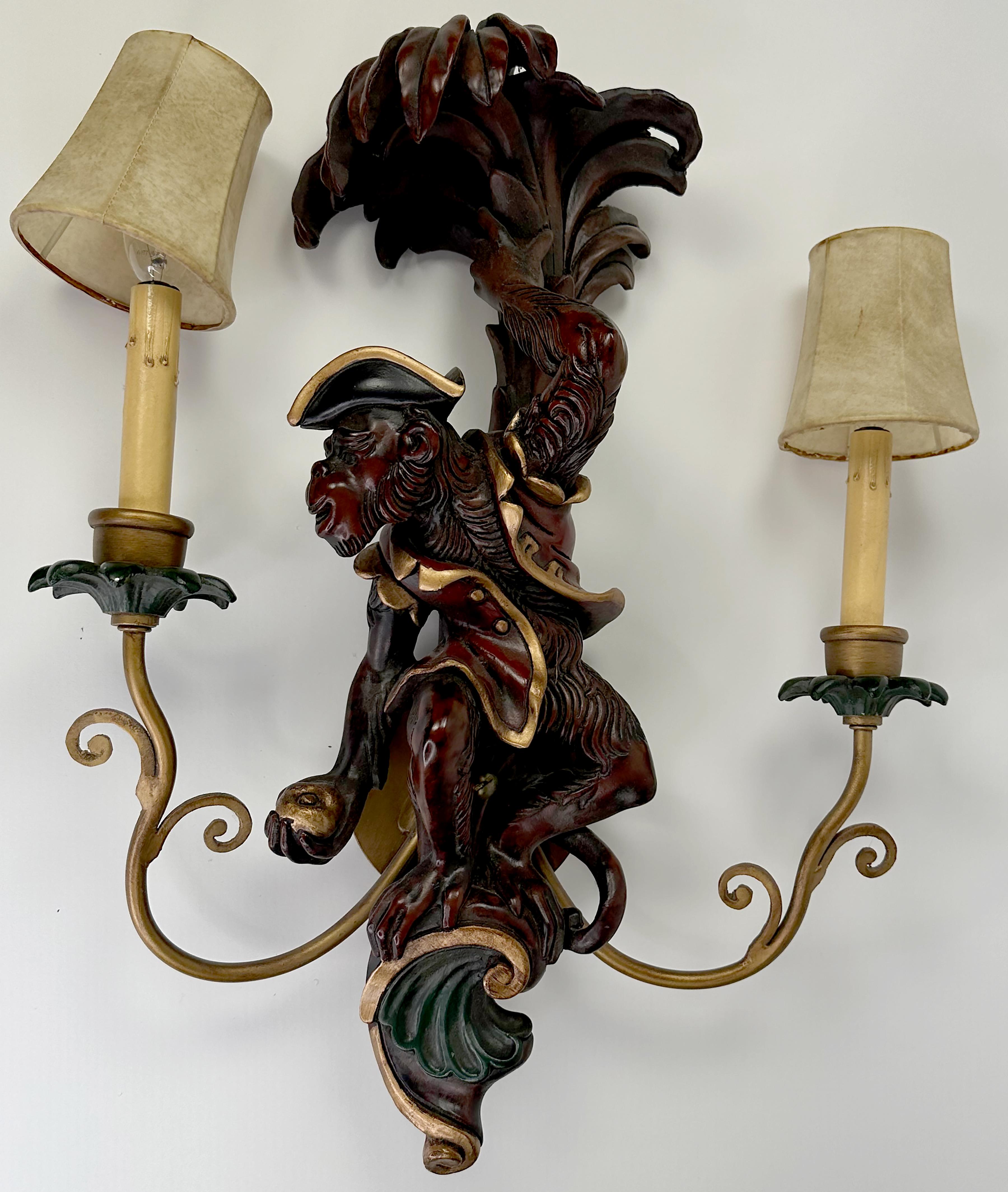 A handsome set of hand-made wall light 2 arm carved wood monkey sconce wall lamps. Hand painted finish with browns, reds and gilt trim. Decorative trim adorns the top above the figures and just below them. The lights stand on curved gilt metal rods