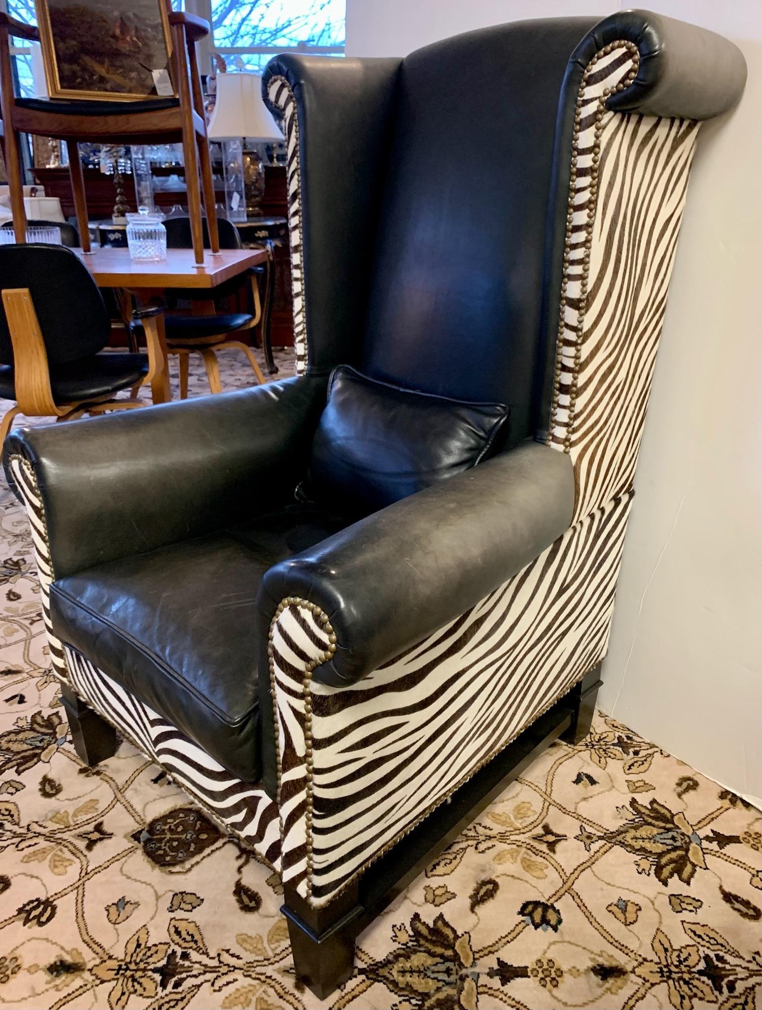 Handsome and very tall custom upholstered modern wingback chair in zebra print cowhide on side, back and front. High quality black leather fabric at from and on arms. Accented with brass nailheads all around. There is some fading in the leather in