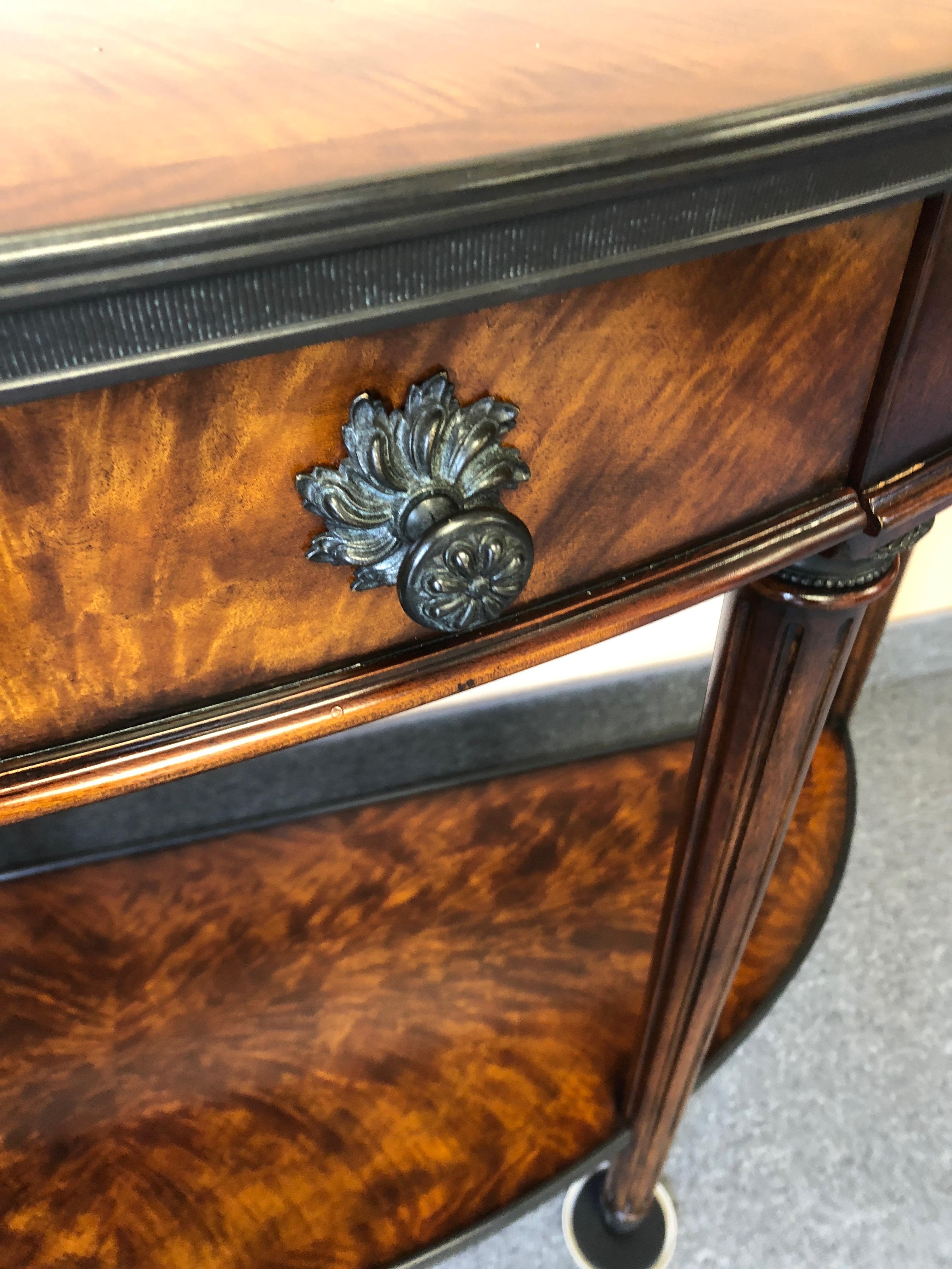 Magnificent bookmatched flame mahogany two-tier demilune console having handsome dark bronze hardware, tapered reeded legs, single drawer and acanthus leaf bronze capped feet.