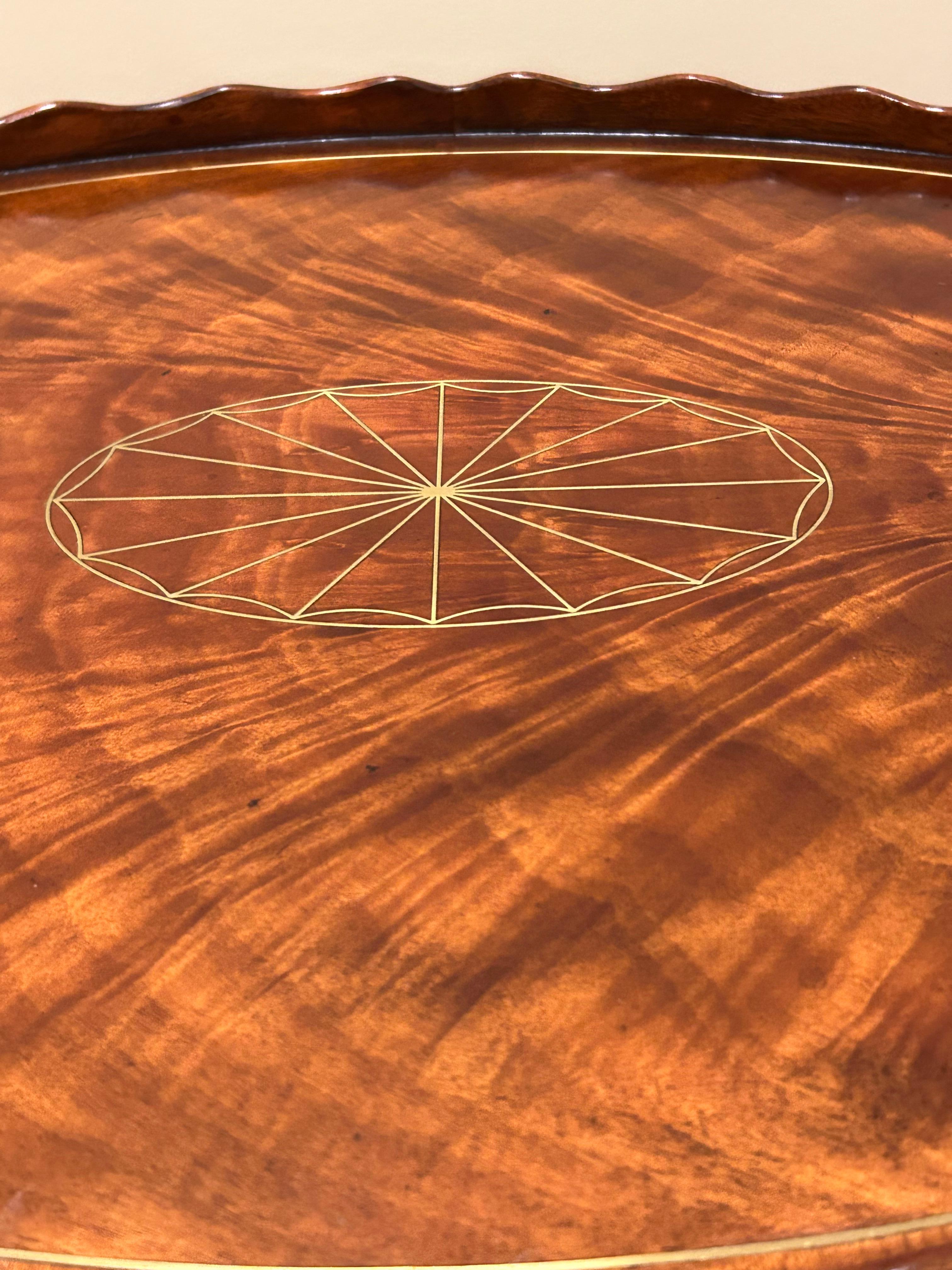 Stunning flame mahogany oval serving tray having elegant brass inlay decoration and rope motif handles. There’s a pie crust undulating gallery as well.