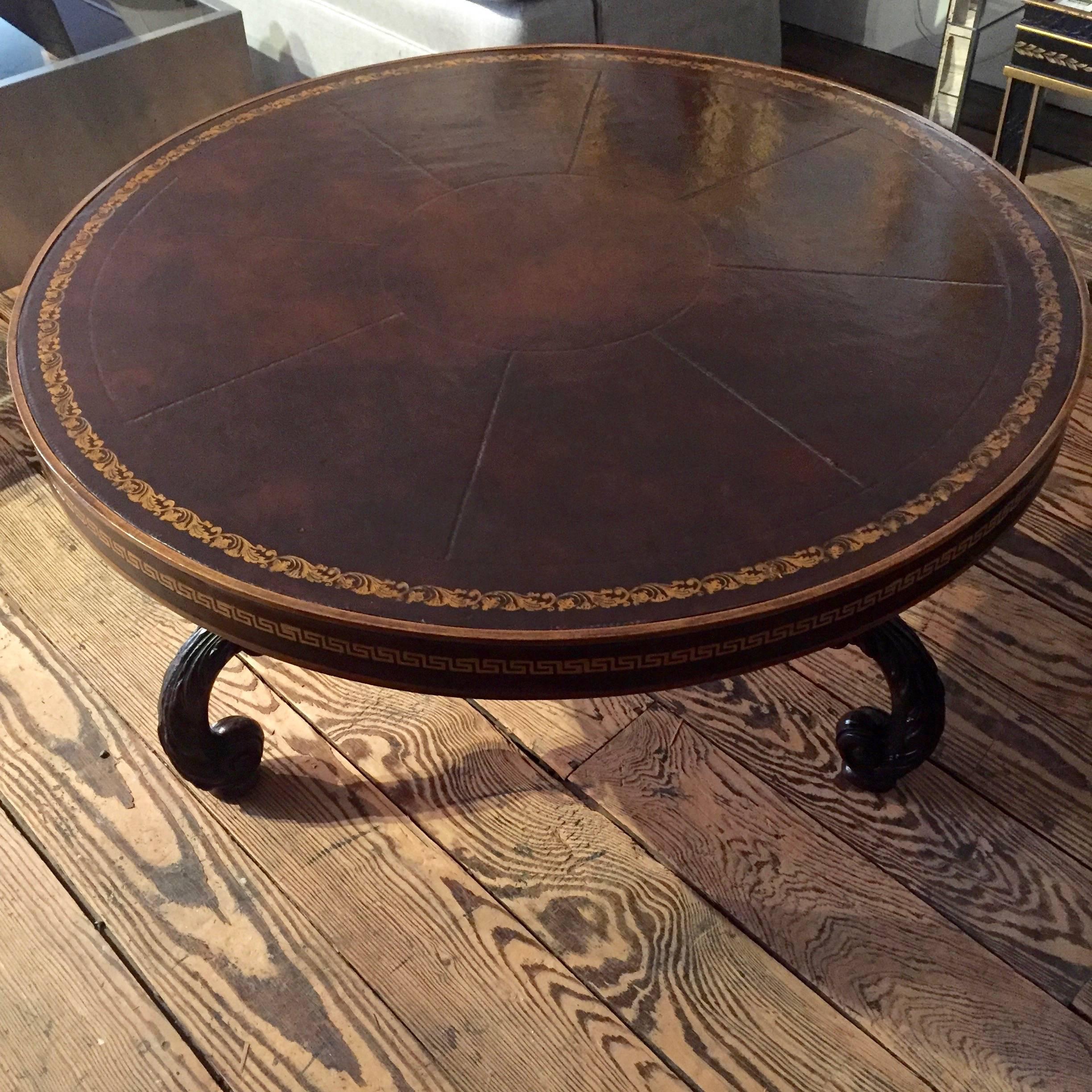 Great looking round coffee table having a stunning tooled leather top with gold embossed design on the periphery and fabulous Greek key decoration on the sides. Base is carved wood with three curvy legs. The top and bottom may not be original to one