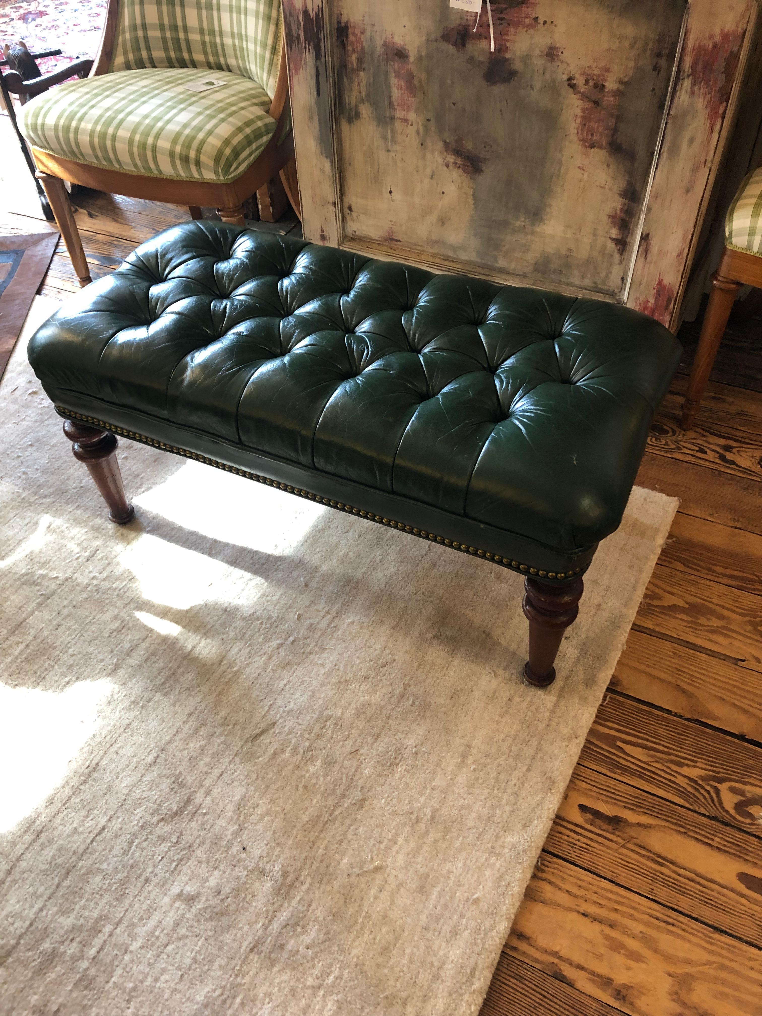 Great medium sized dark green leather tufted bench having handsome turned walnut legs and brass nailhead detailing.