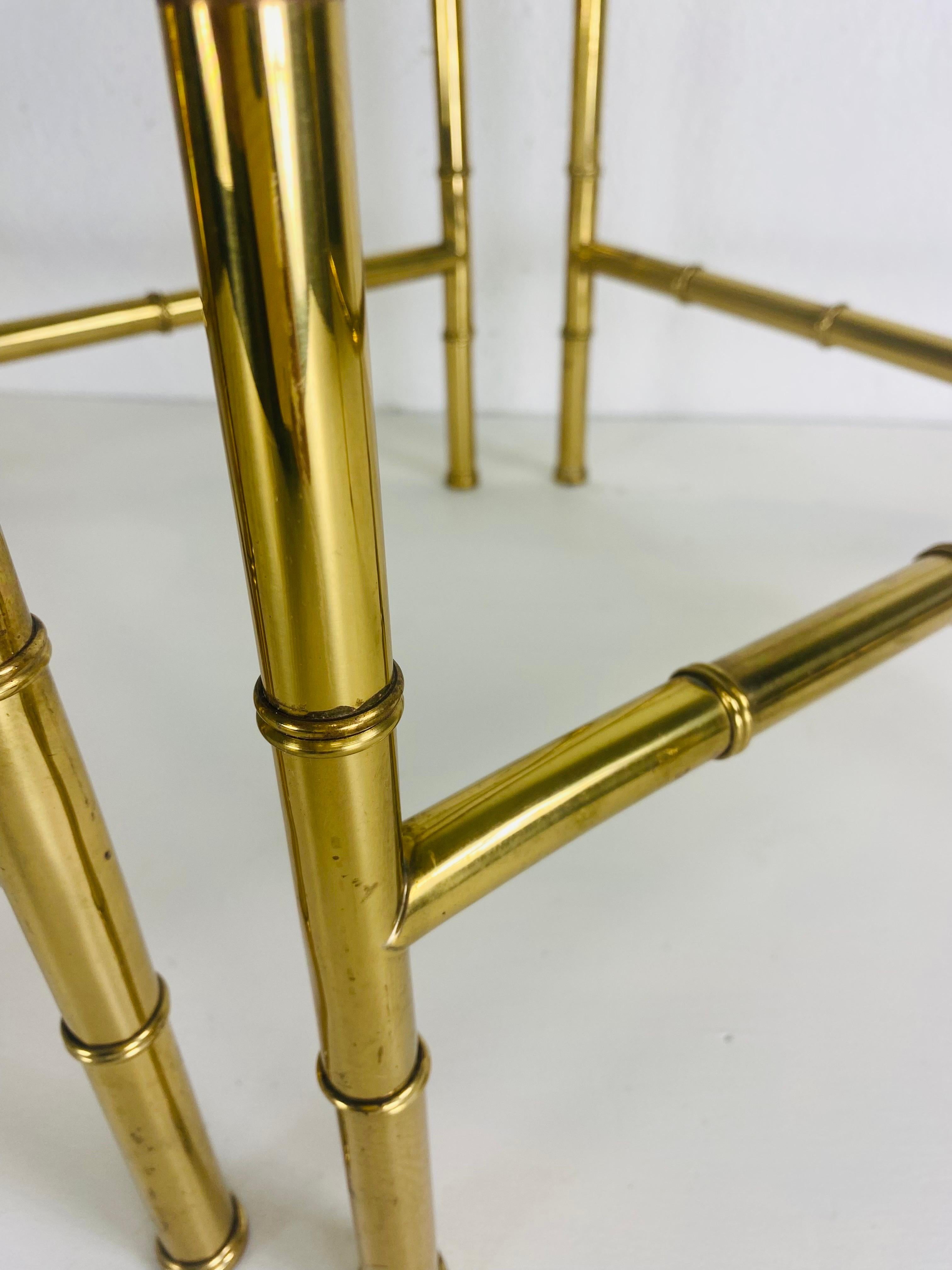 This is a pair of super chic solid brass Regency inspired side tables. This pair of clean streamline side tables features the original heavy glass table top. The tables have a faux bamboo leg and cross stretchers with a clean straight line at the