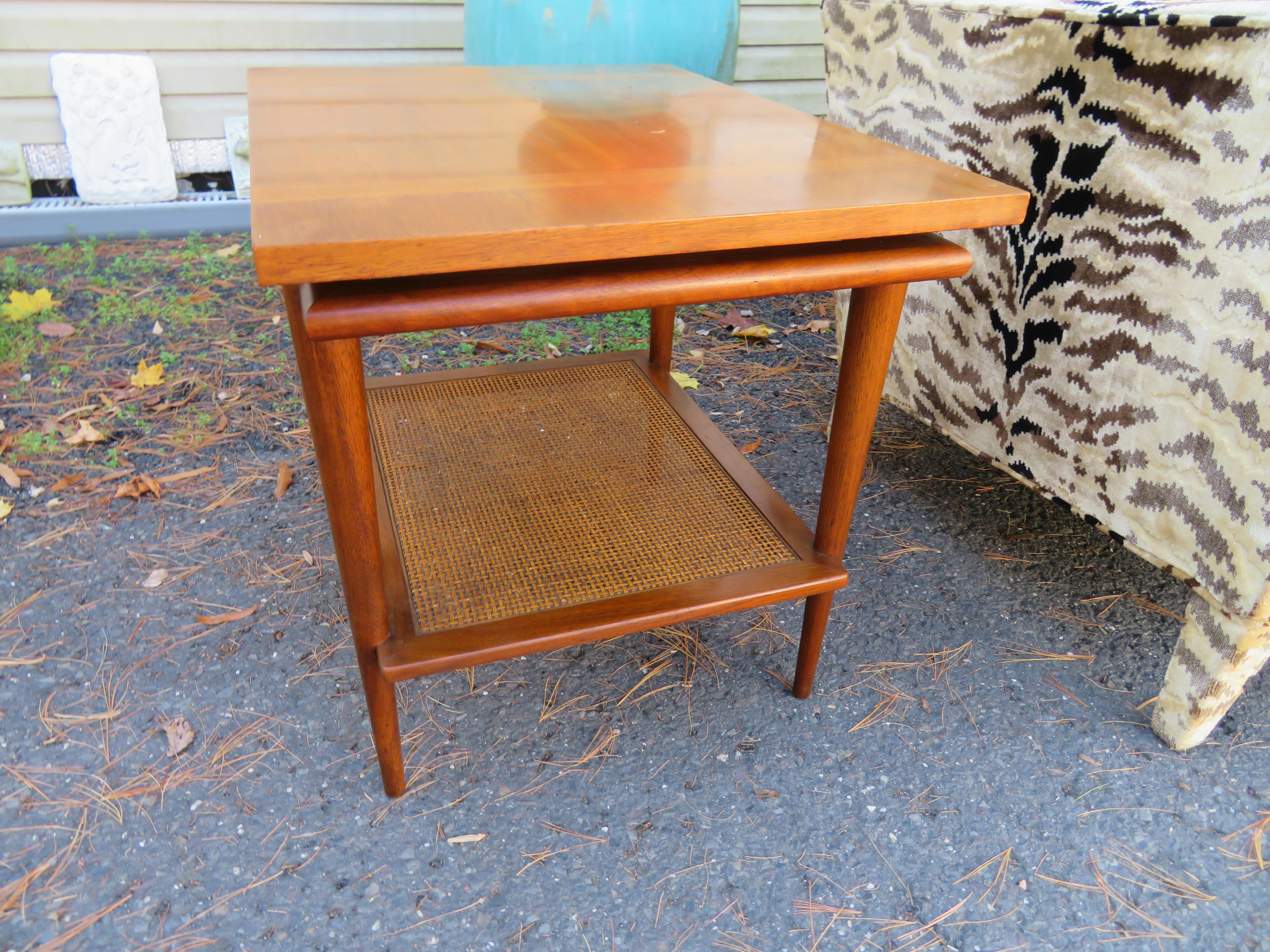 A vintage 1960s Mid-Century Modern end table with floating top and caning by John Widdicomb. This handsome occasional table features a rectangular top floating over a base with tapering legs and a caned magazine shelf. Works well with Danish or