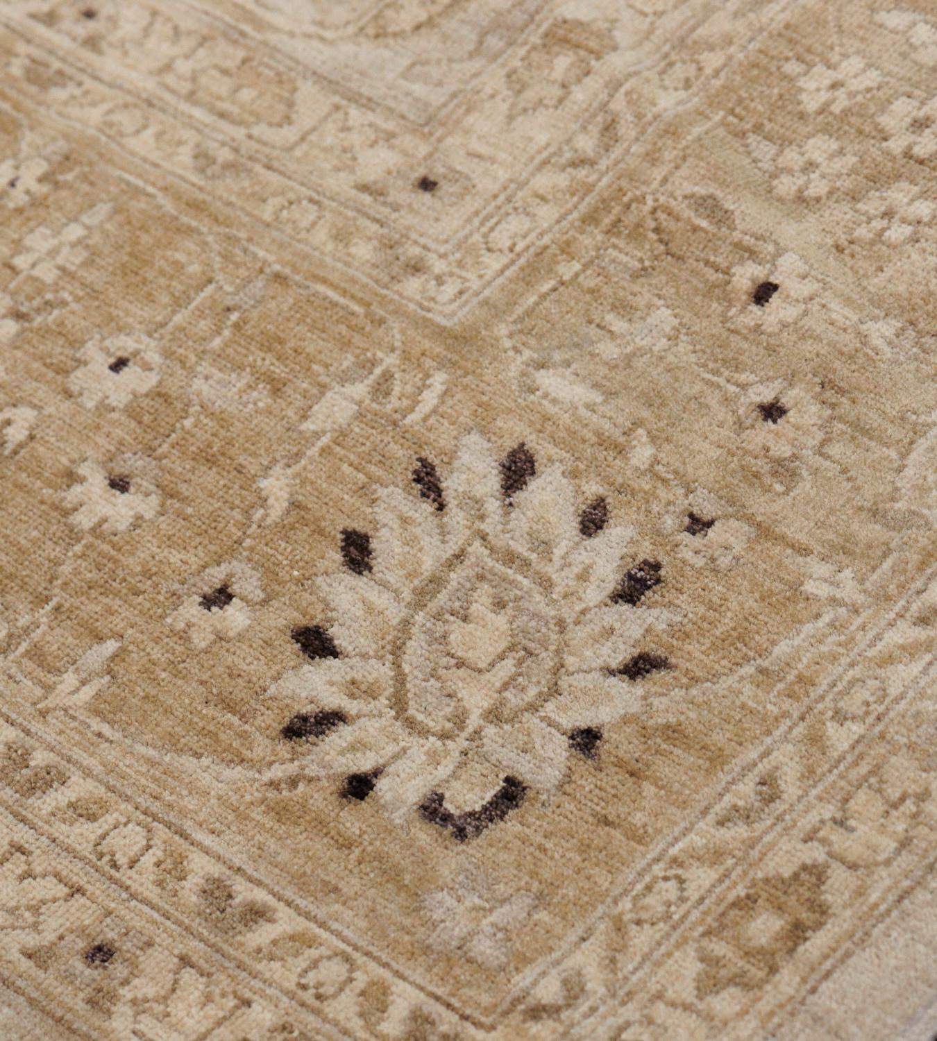 This handwoven reproduction Indian Agra rug has an overall beige field with tonal wandering palmette vines issuing fine floral motif, issued by a central suggested cusped lozenge, in a fox brown palmette vine border, between elegant complementary