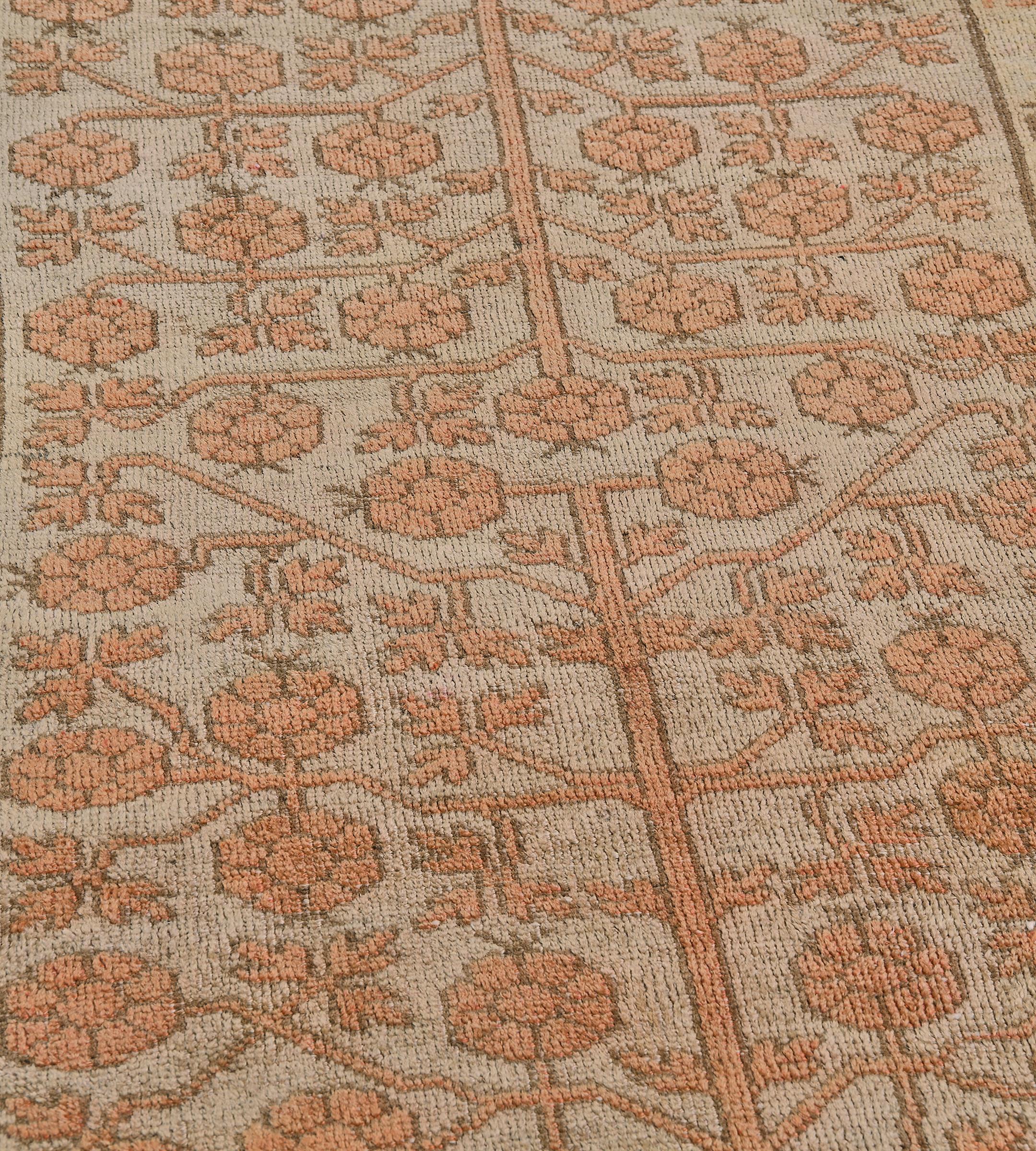 This antique Khotan runner has a shaded buff-brown field with an overall design with a terracotta-orange vase at each end issuing an angular vine linking bold pomegranates and leafy sprays, in a golden-yellow border of shaded mole-brown and