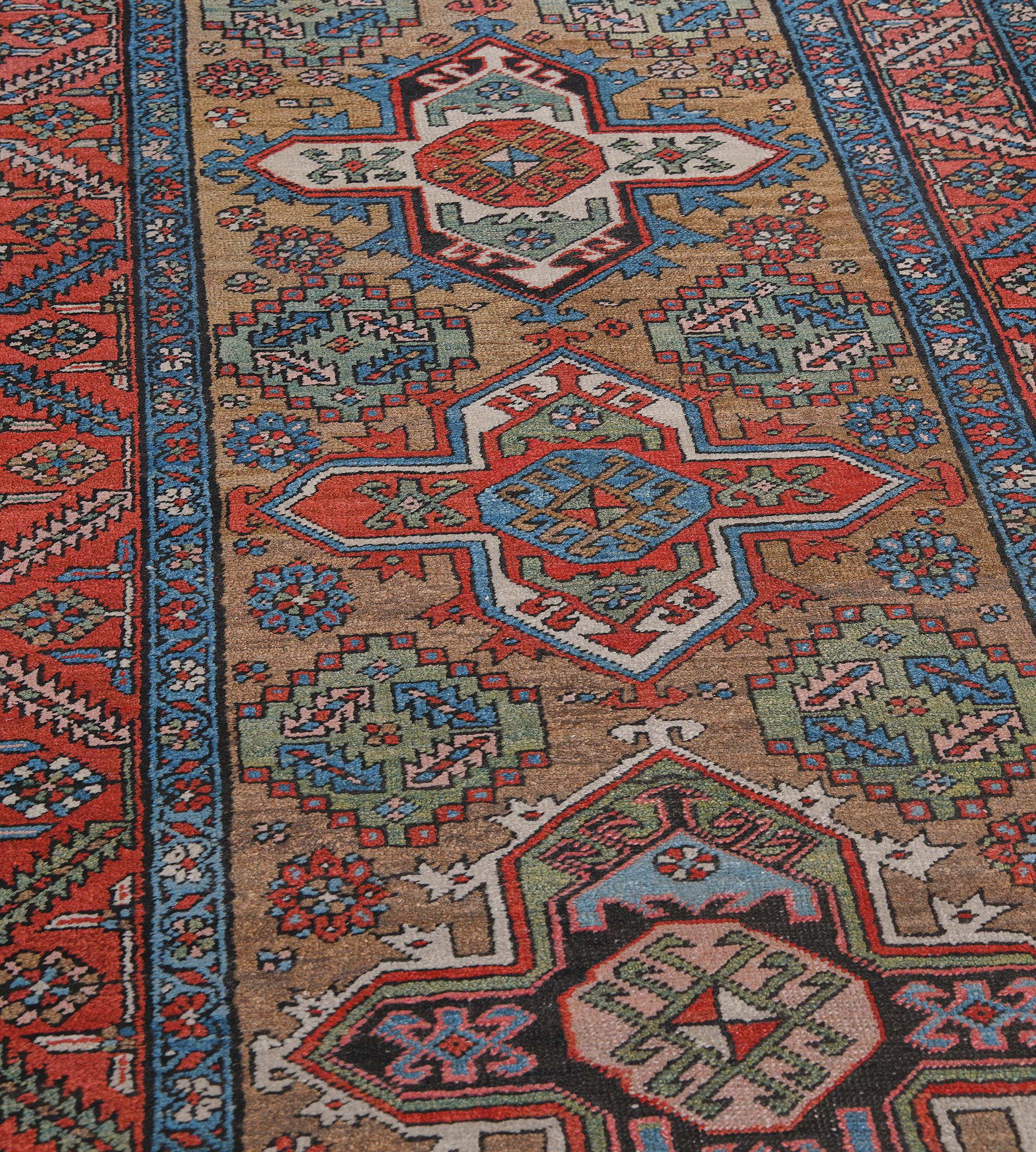 Dieser antike persische Heriz-Läufer hat ein kamelbraunes Feld mit einer Säule aus zwölf polychromen, hakenförmigen und miteinander verbundenen Rauten, die jeweils eine zentrale Blumentafel mit eckigen Pflanzenmotiven enthalten. Die Rauten sind von