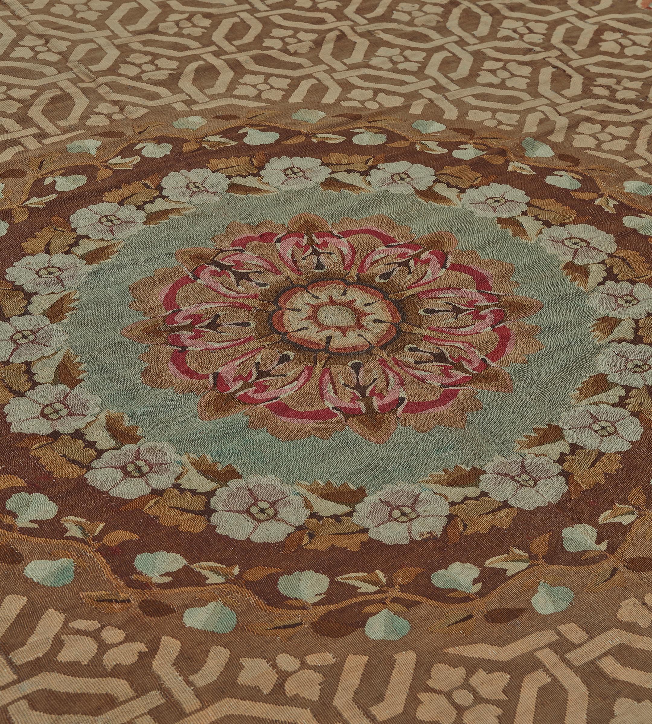 Questo antico tappeto Aubusson francese del 1850 circa ha un campo marrone volpe con un motivo esagonale a incastro marrone sabbia che racchiude un fiore a quattro petali, un bouquet floreale in ogni angolo, il tondo centrale con bande floreali e