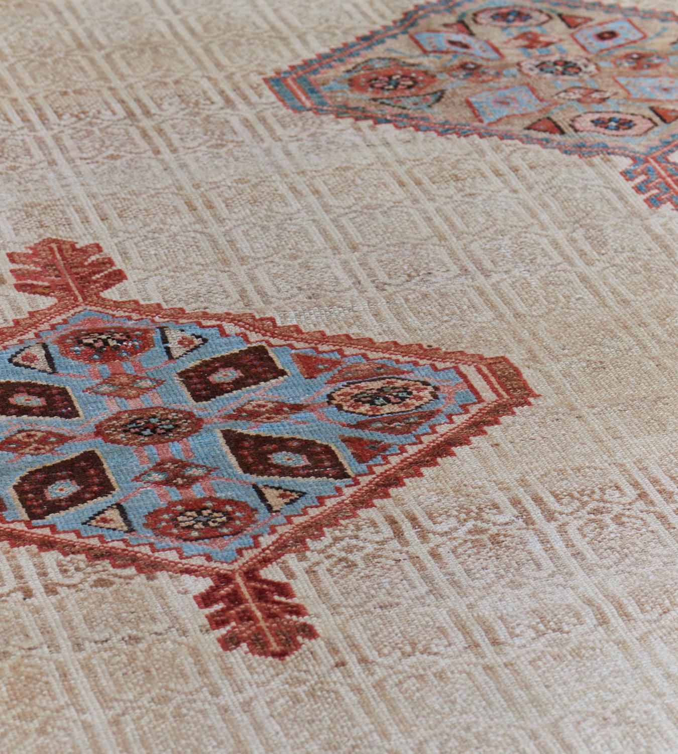 This antique, circa 1890, hand-woven Serab Persian rug has an ivory field with a light brown vertical trellis of linked paired both around diagonal rows of spaced serrated light blue and sandy-brown lozenges and part lozenges with leaf pendants each