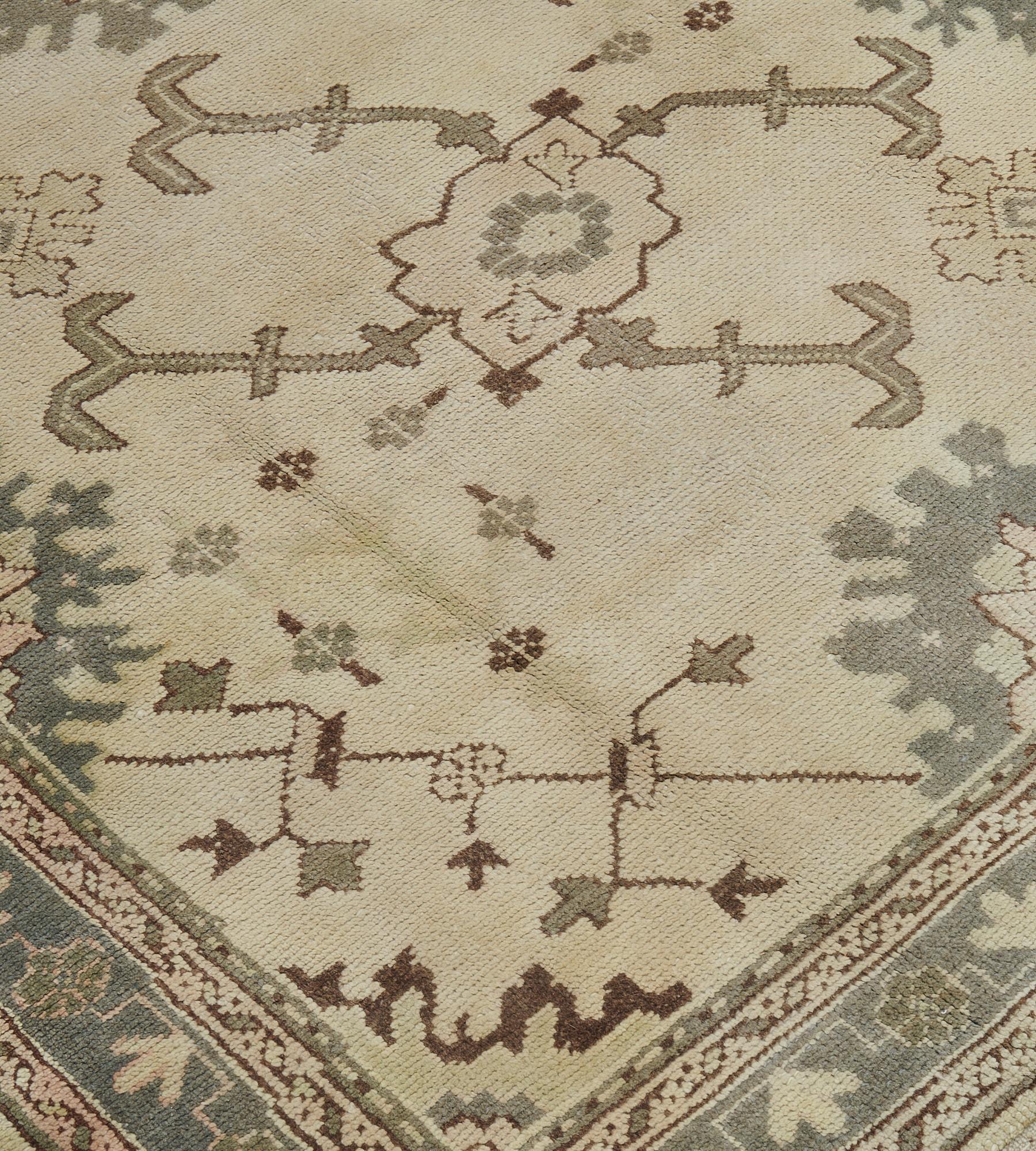 Ce tapis Oushak ancien, vers 1900, a un champ ivoire nuancé avec un médaillon central en losange étagé contenant une tête de fleur émettant des tiges crochetées gris doux entourées d'une variété de têtes de fleurs et d'autres palmettes cuspidées,